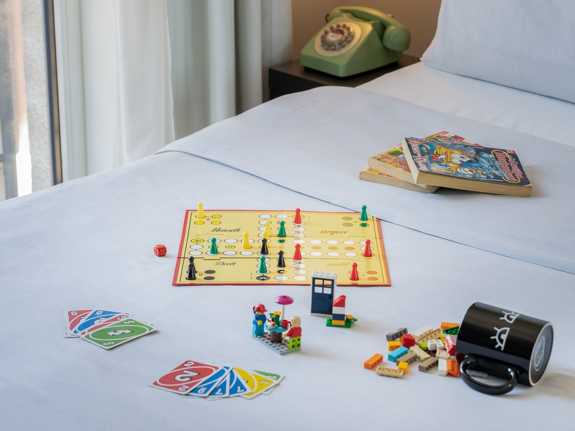 Board game, Uno cards, Lego, books, and green rotary phone on a bed.