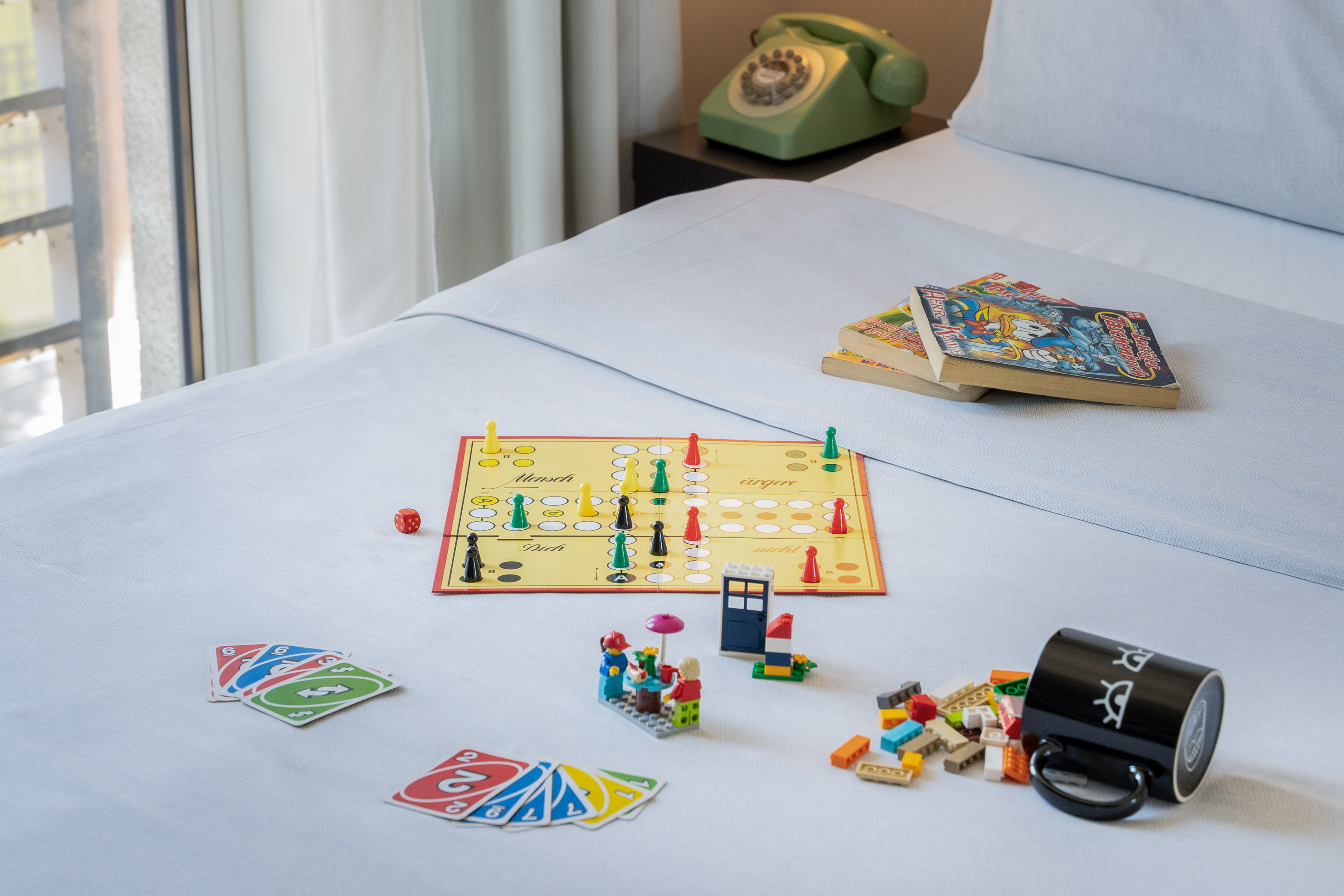 Board game, Uno cards, Lego, books, and green rotary phone on a bed.