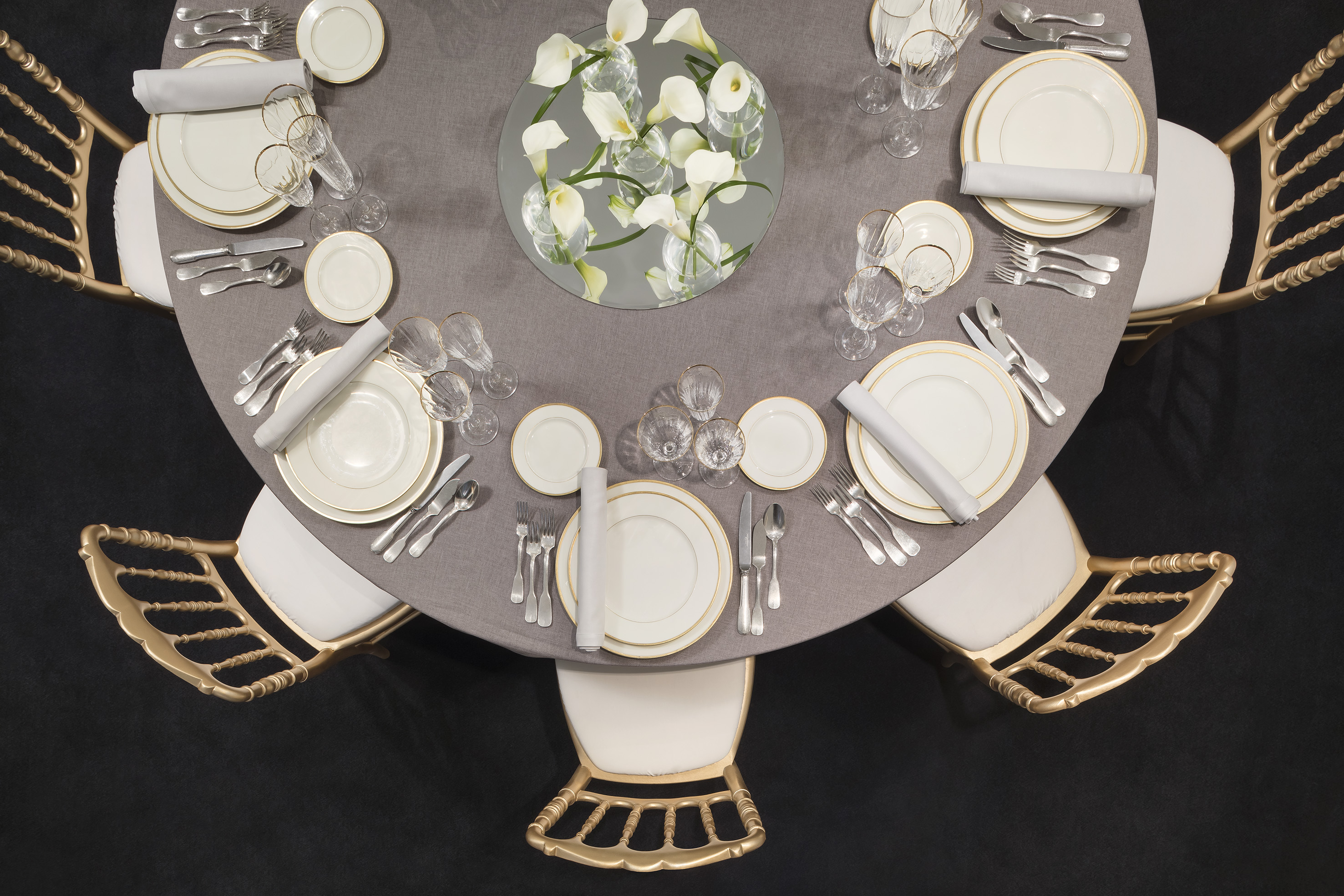 Formal dining table with gold-rimmed plates, calla lilies, gold chairs.
