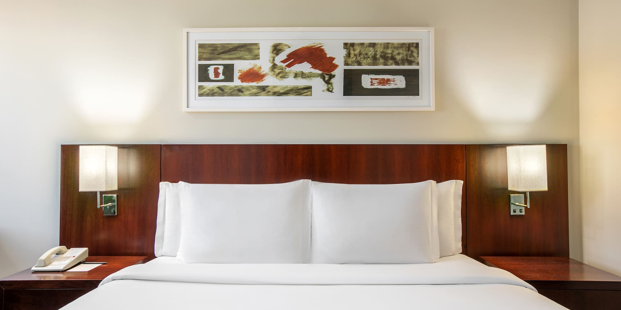 a bed with white sheets and a painting above it