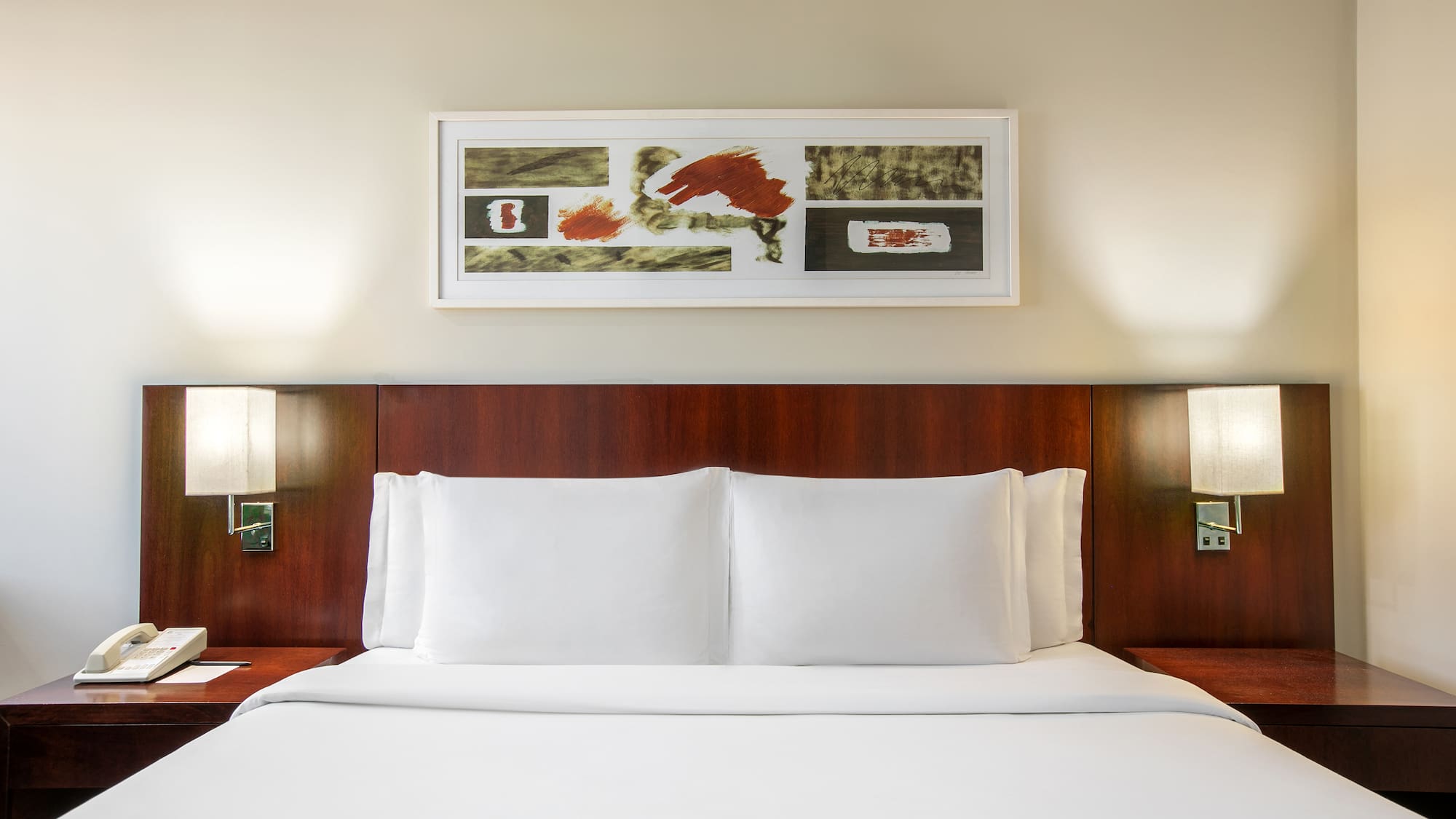 a bed with white sheets and a painting above it