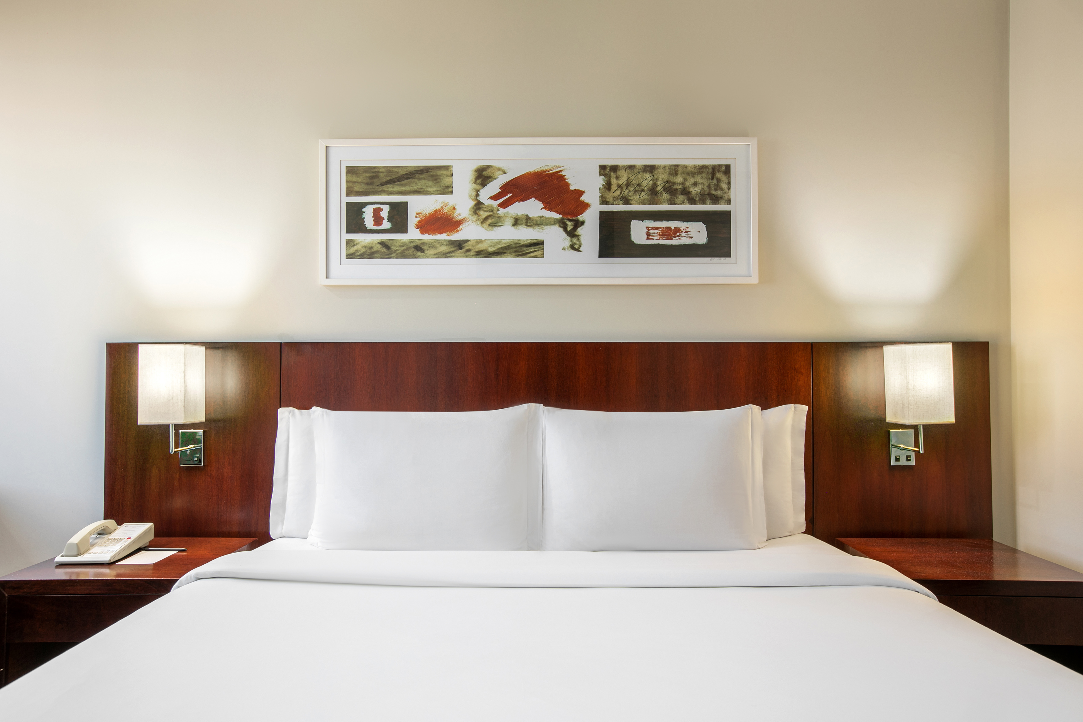 Hotel room bed with white linens, dark wood headboard, and bedside lamps.