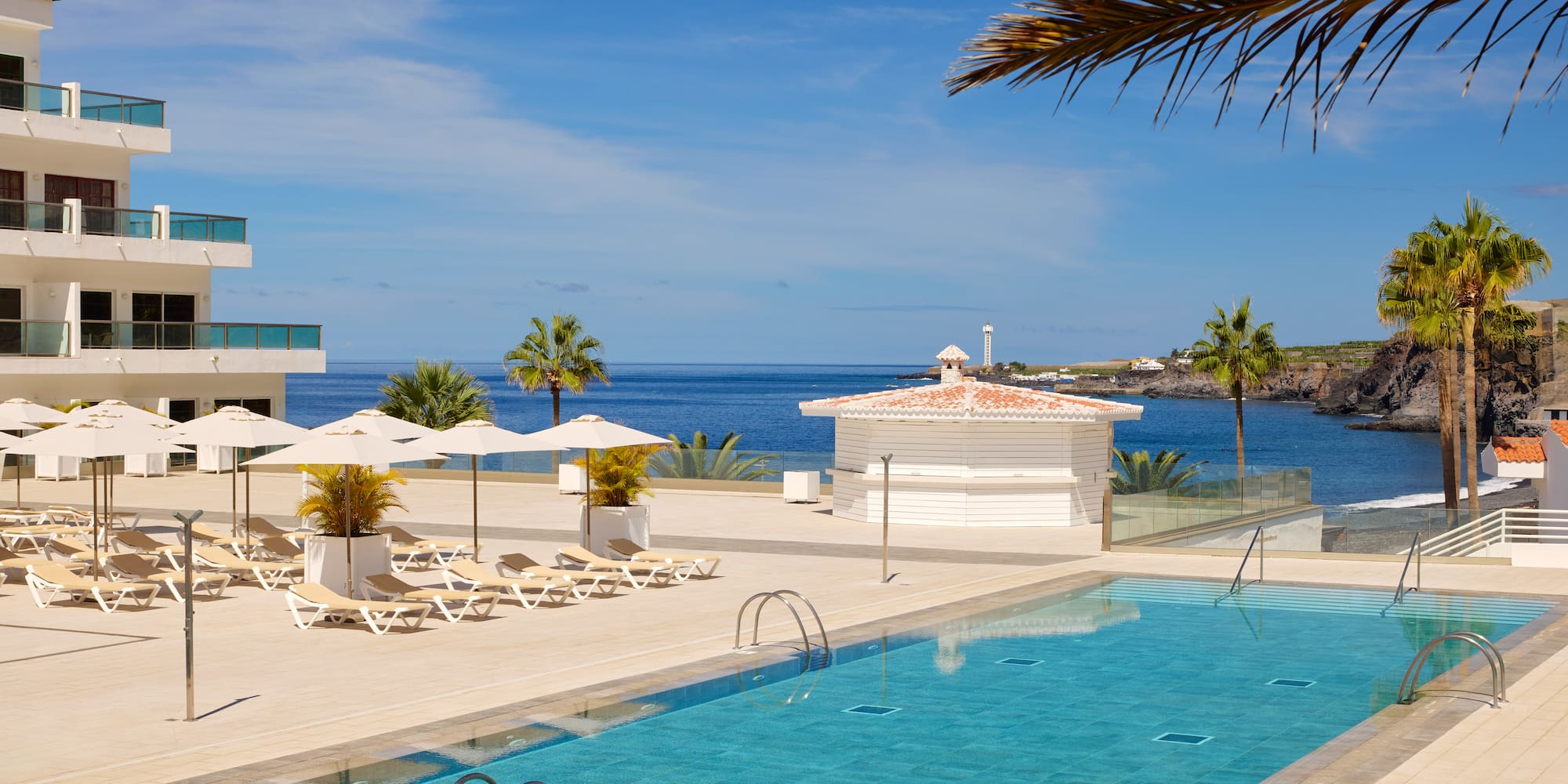 a swimming pool with chairs and umbrellas by a building