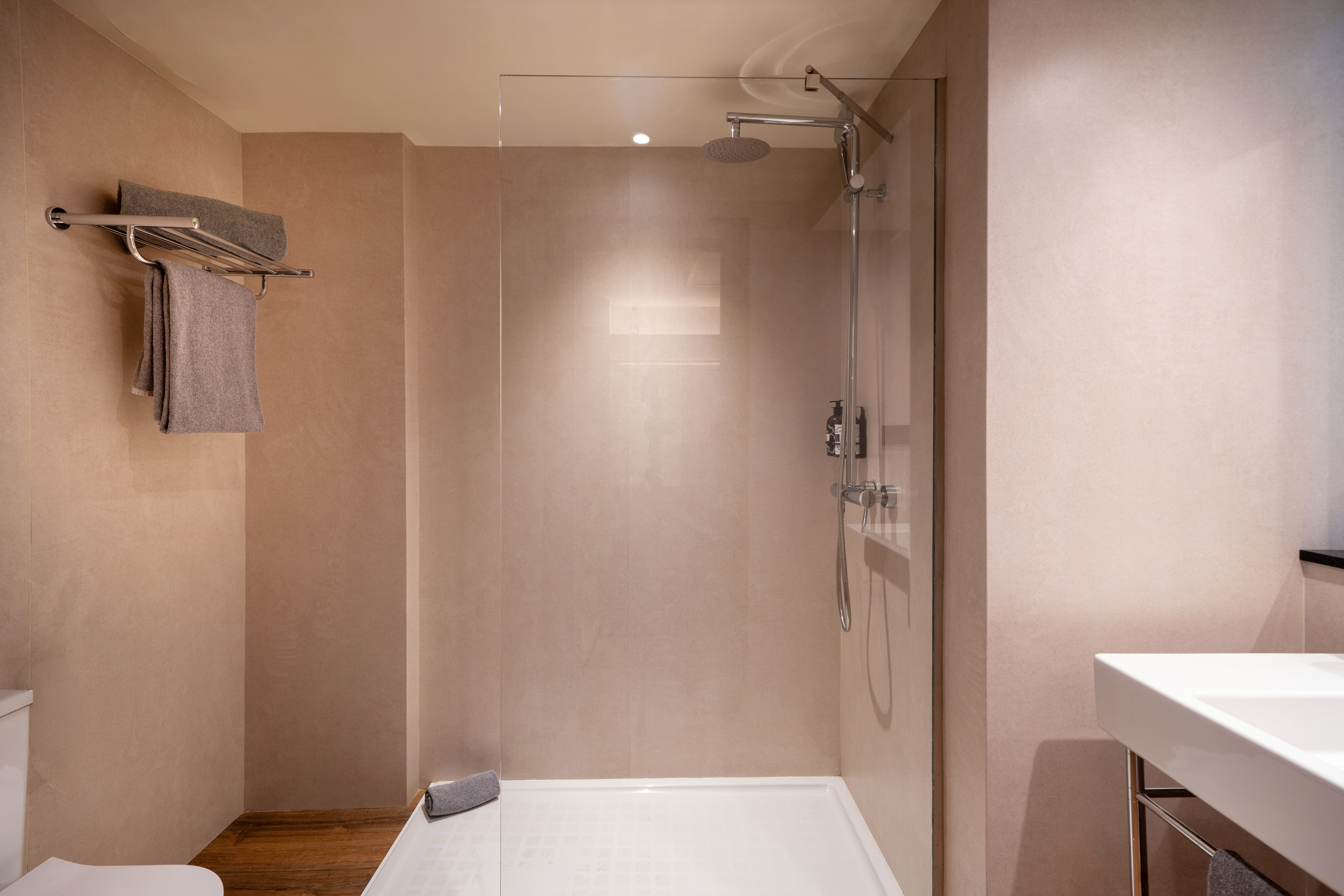 Modern hotel bathroom with glass shower, rain head, towel rack, and sink.