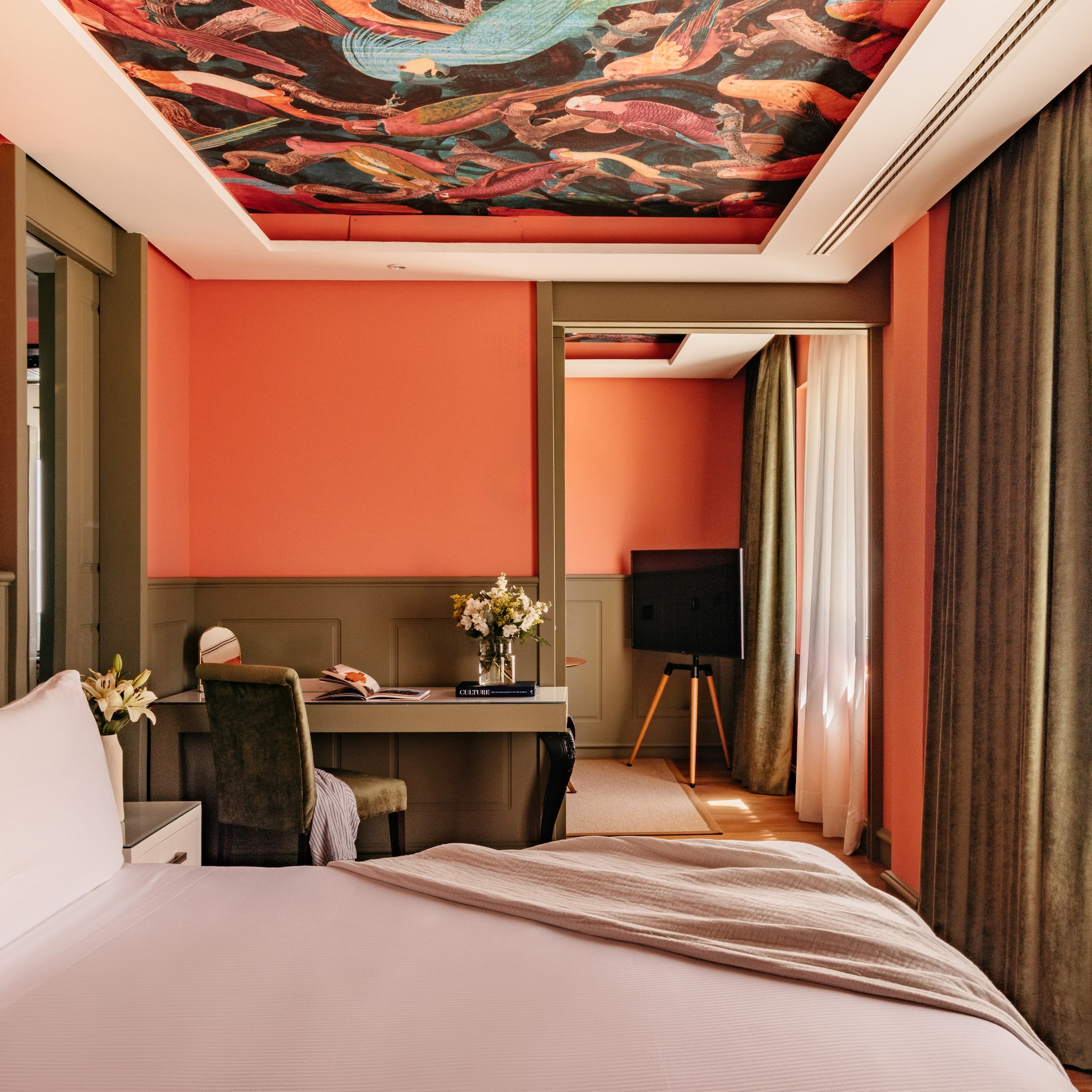Habitación de hotel con paredes coral, techo mural y cama blanca.