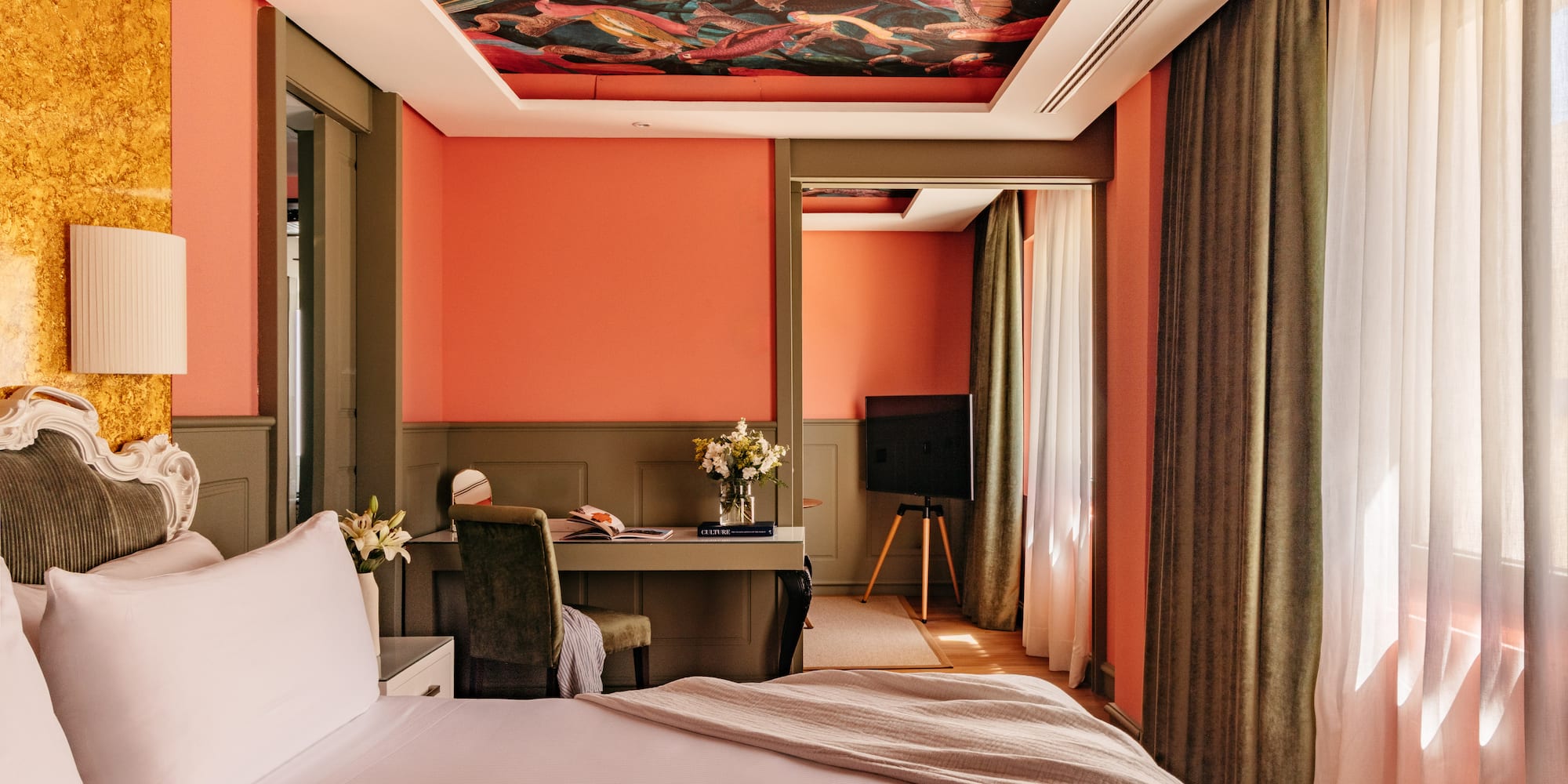 Habitación de hotel con paredes coral, techo mural y cama blanca.