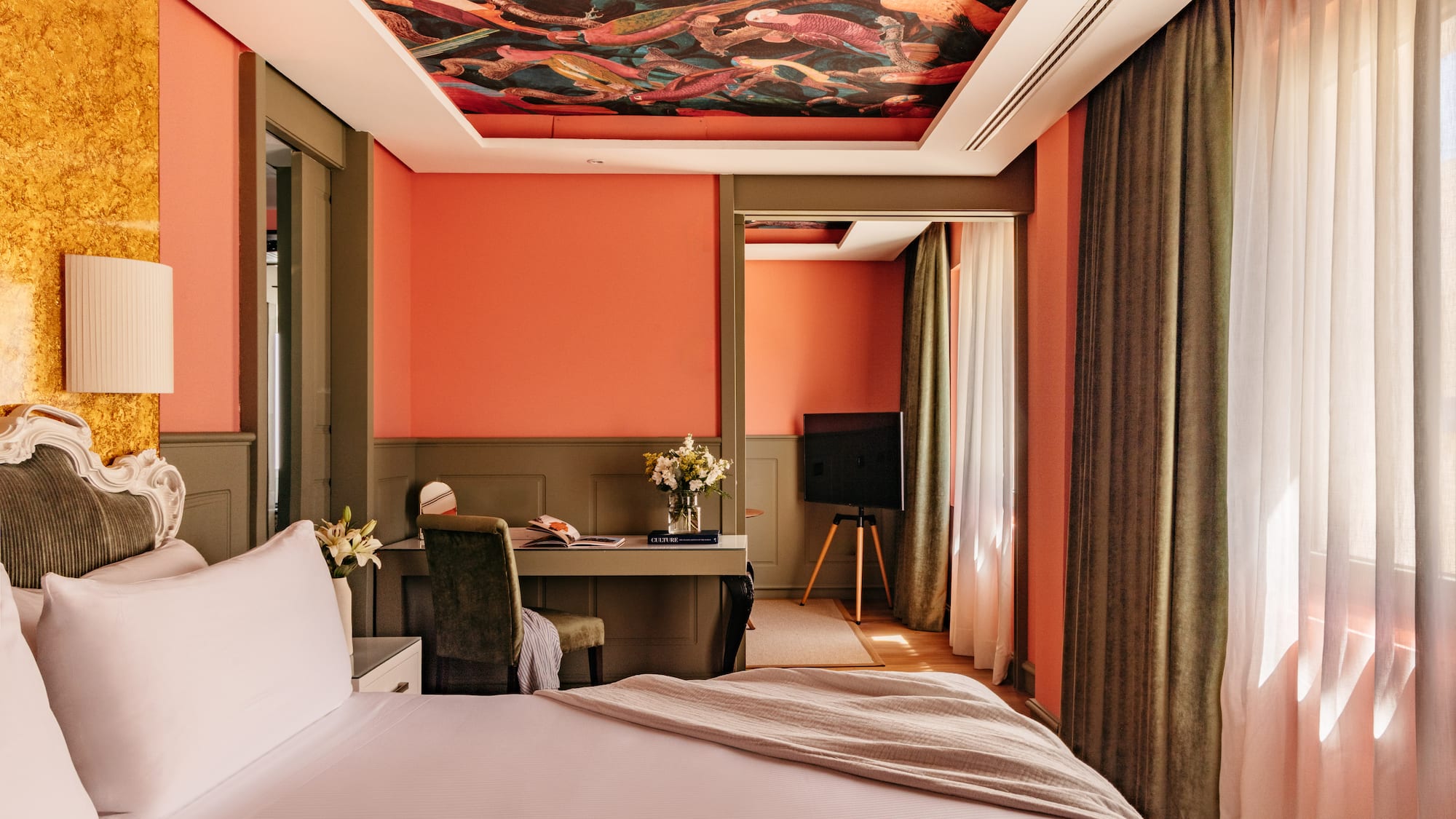 Habitación de hotel con paredes coral, techo mural y cama blanca.