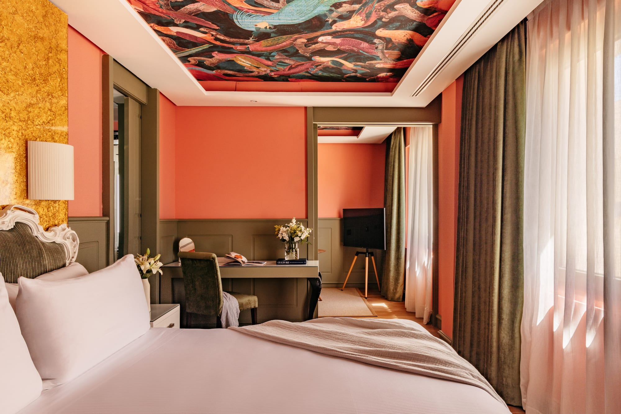 Habitación de hotel con paredes coral, techo mural y cama blanca.