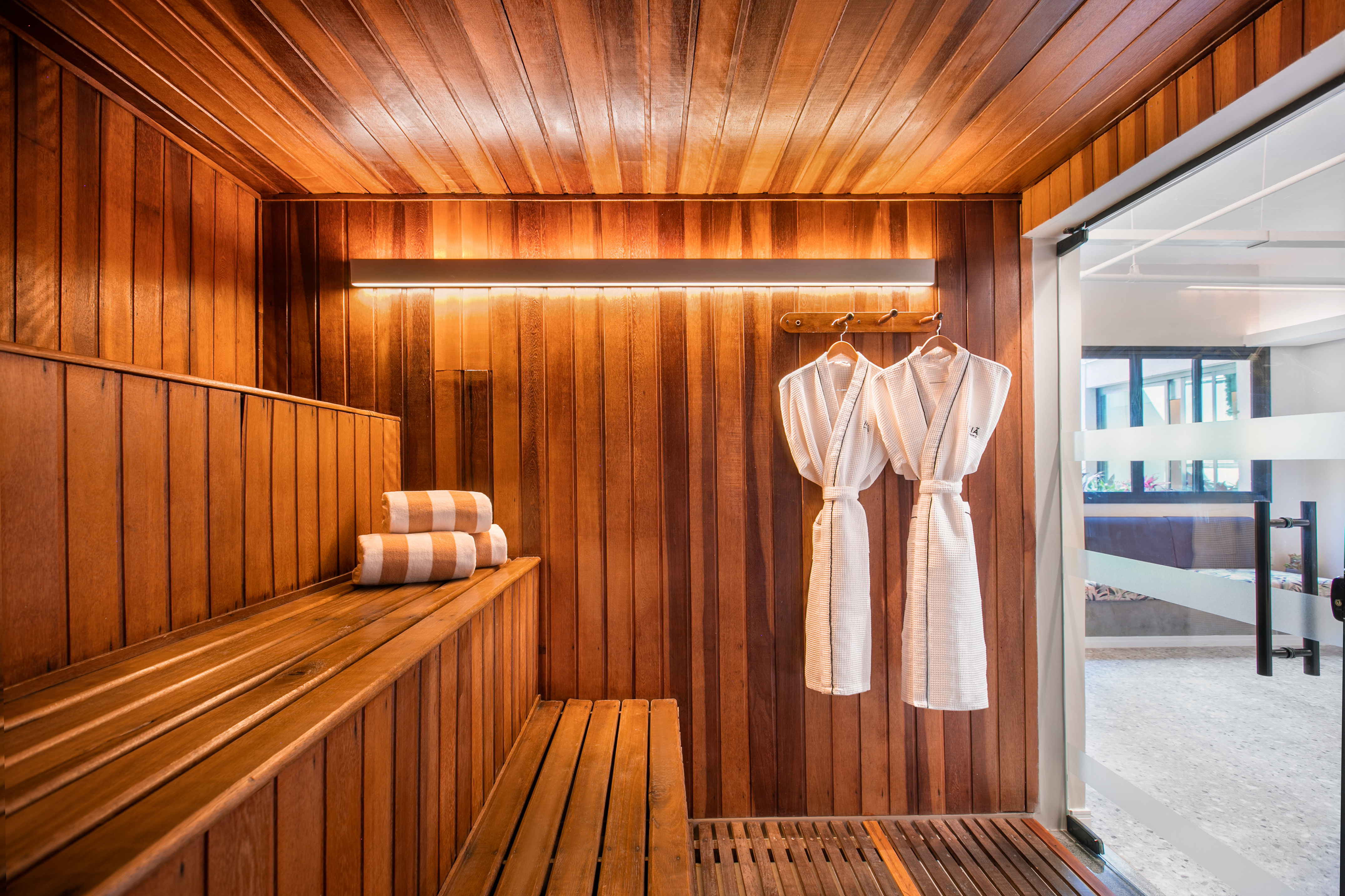 Wooden spa sauna with benches, hanging bathrobes, and striped towels.