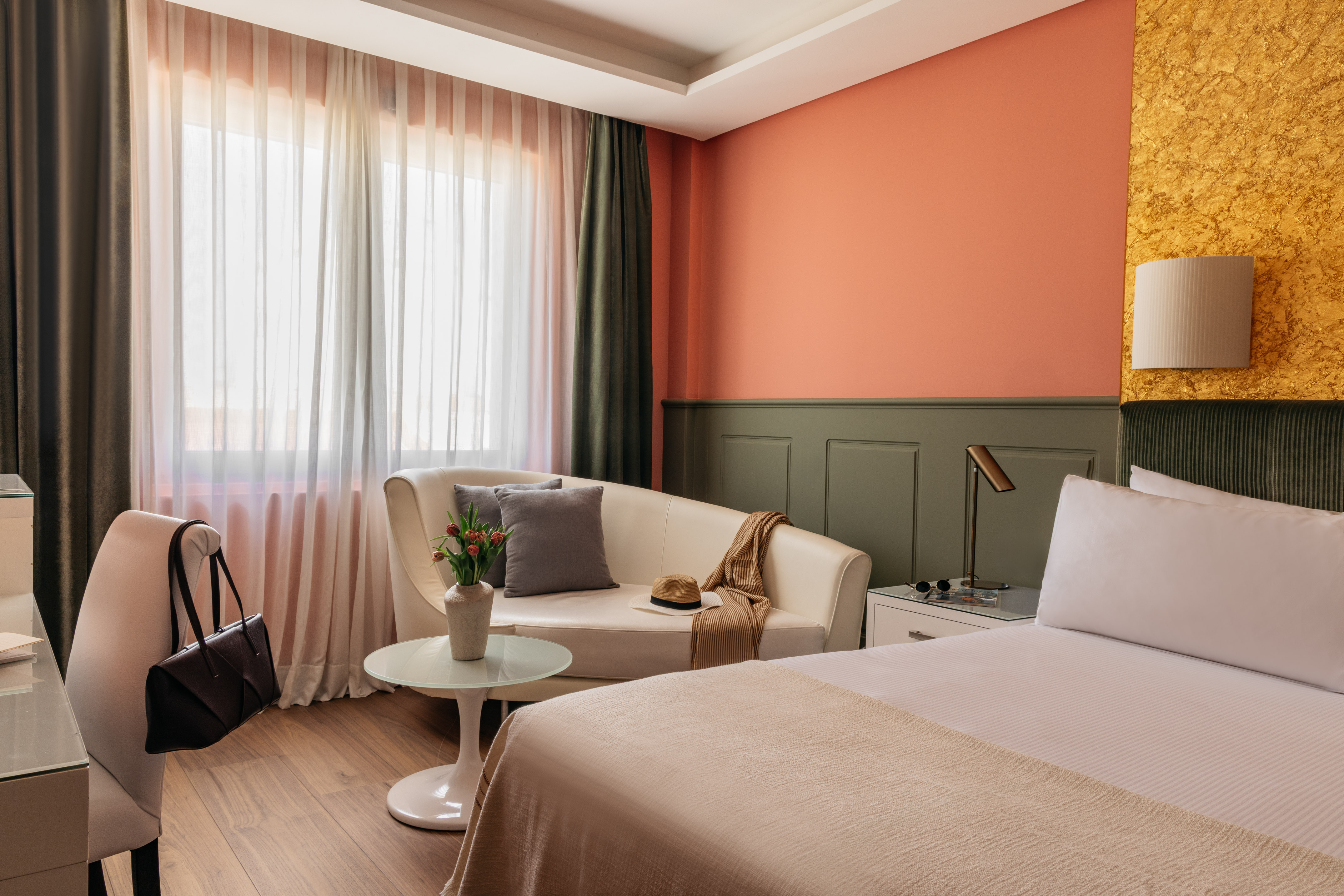 Boutique hotel room with bed, white sofa, vibrant coral and gold accent walls.