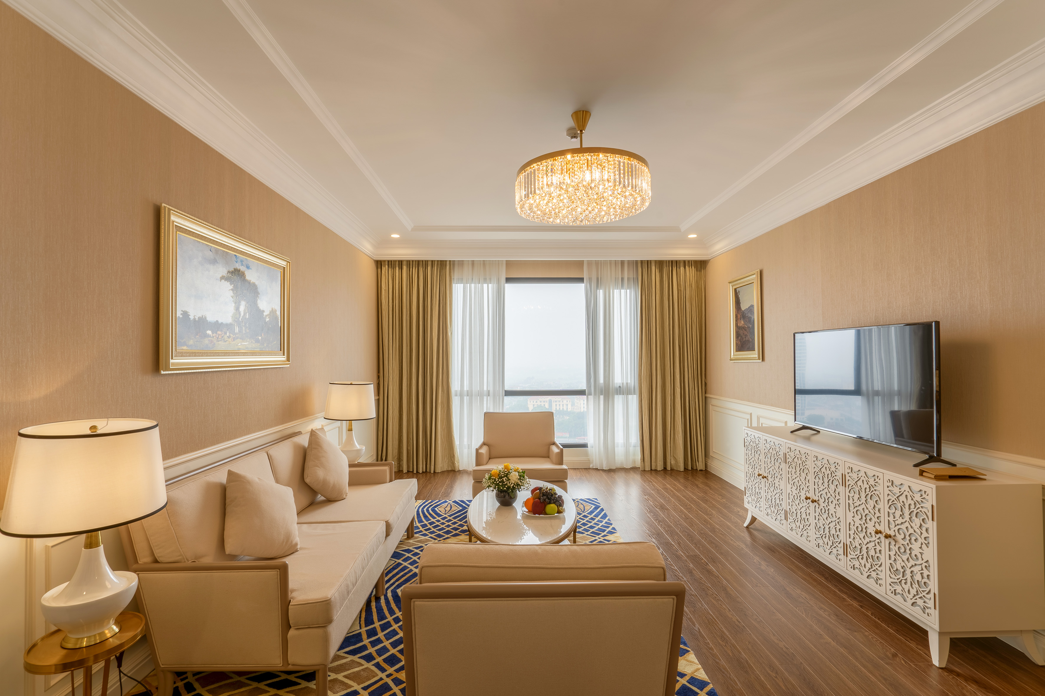 Spacious luxury living room with beige sofa, chandelier, city view, and TV.