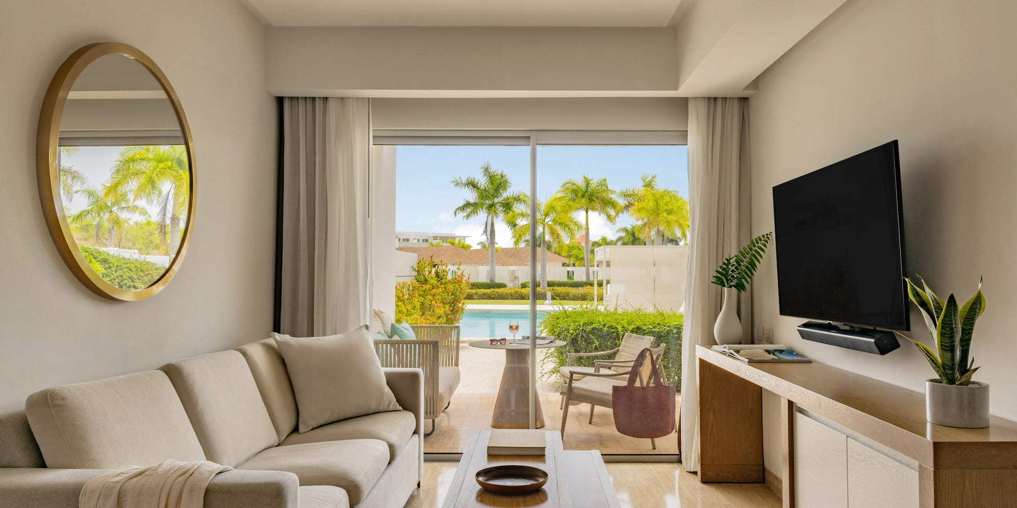 Bright living room opens to private pool and tropical patio with palm trees.
