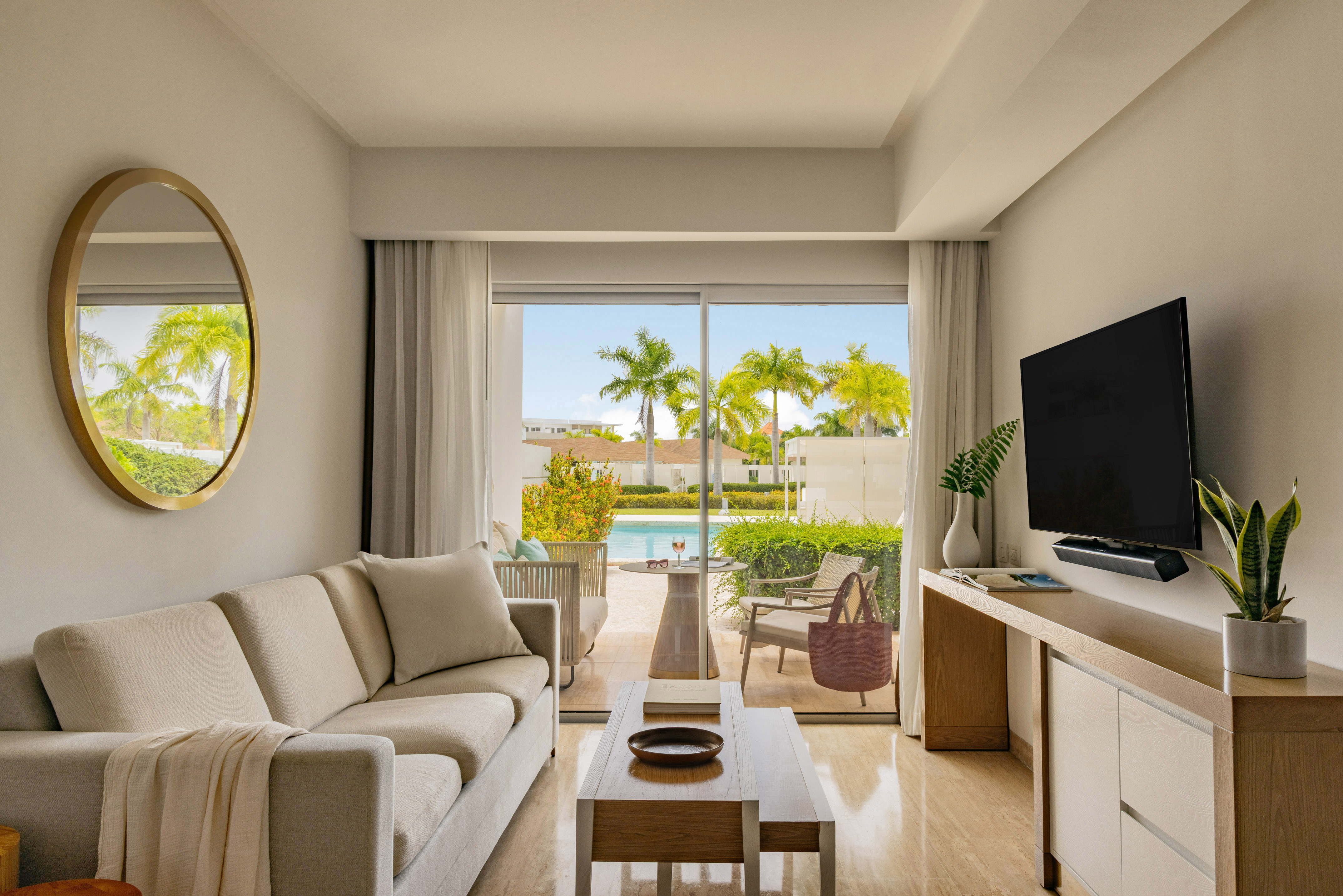Bright living room opens to private pool and tropical patio with palm trees.