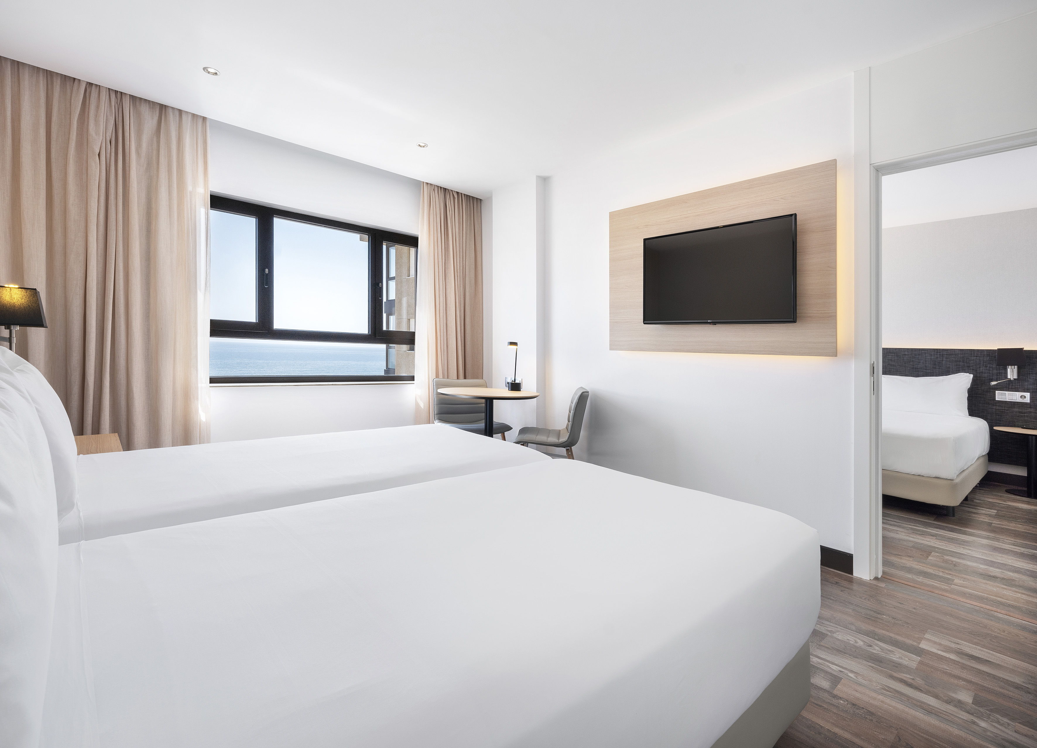 Modern hotel room with twin beds, ocean view, and wall-mounted TV.