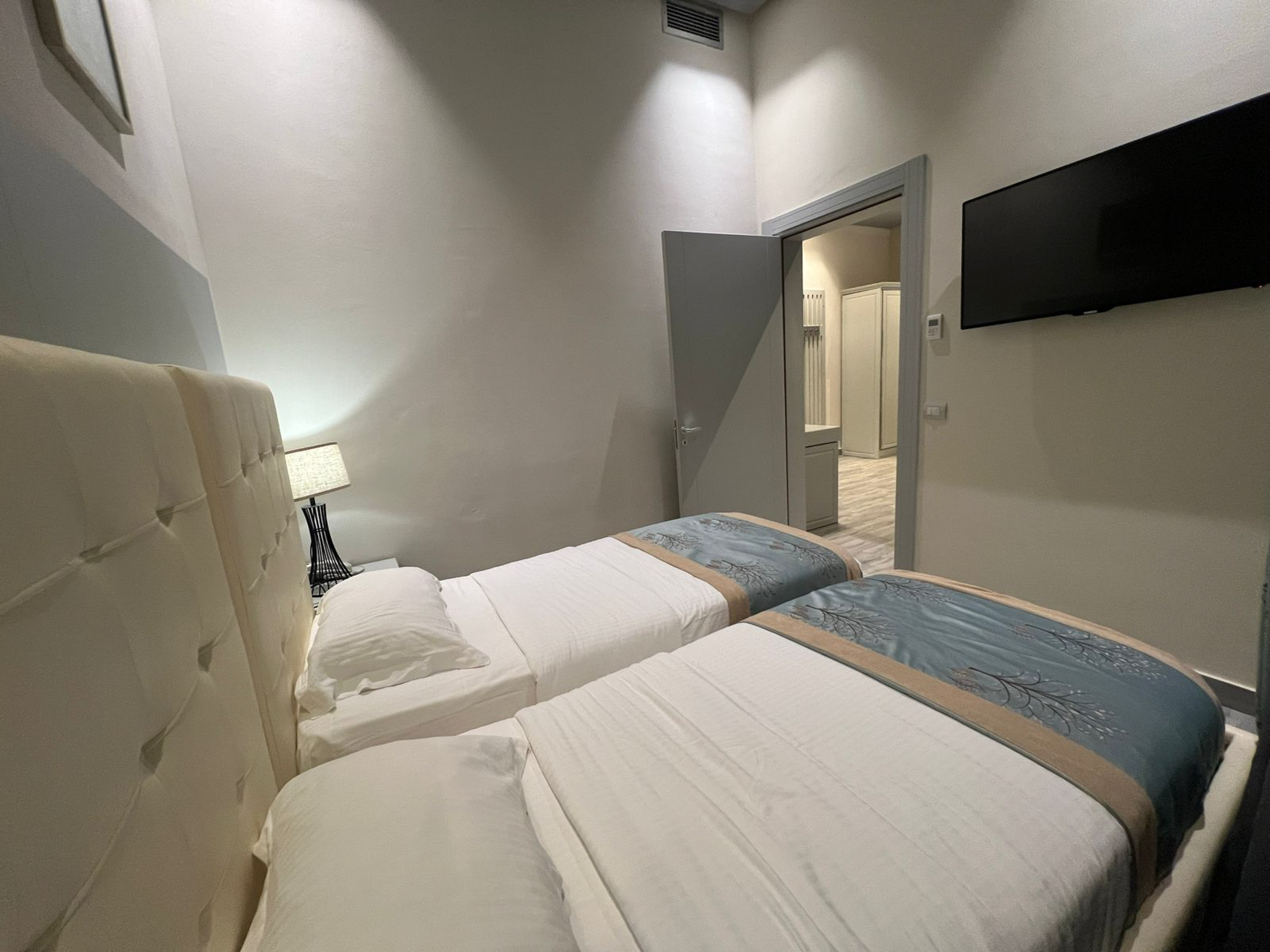 Twin beds in a modern guest bedroom with lamp and wall TV.