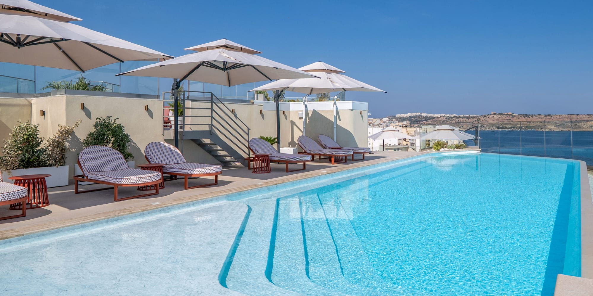 Rooftop swimming pool with lounge chairs, parasols, and ocean view.