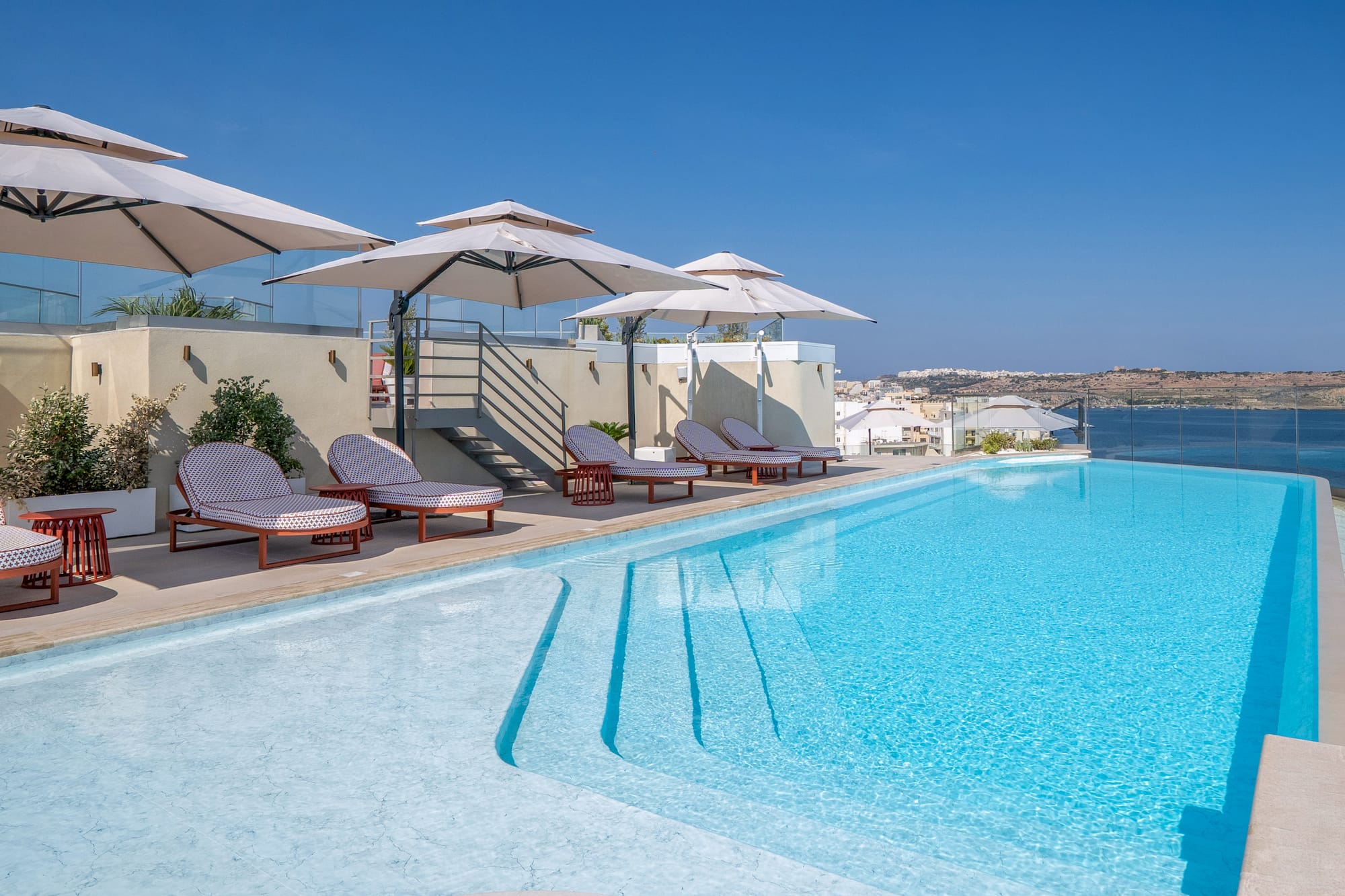Rooftop swimming pool with lounge chairs, parasols, and ocean view.