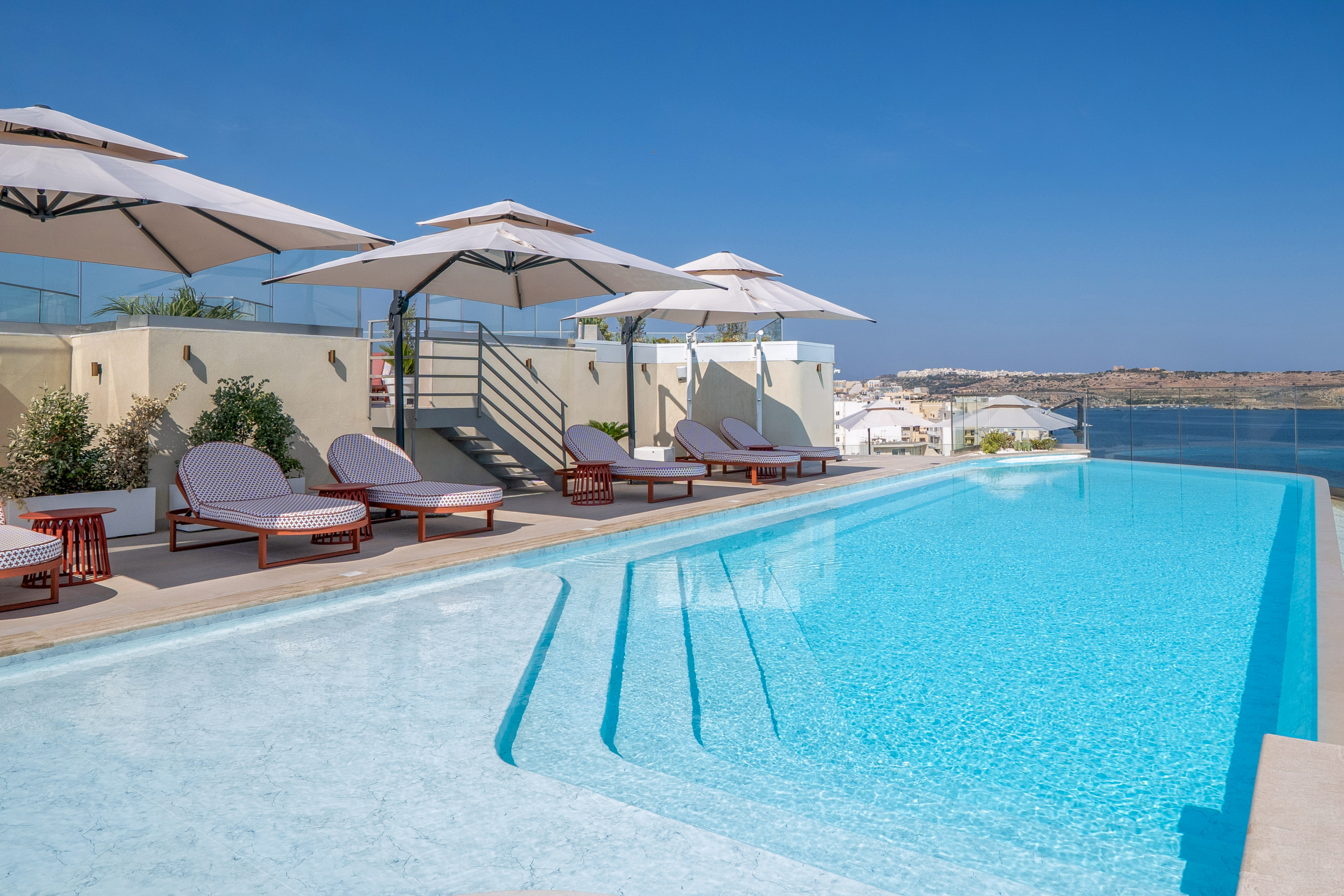 Rooftop swimming pool with lounge chairs, parasols, and ocean view.
