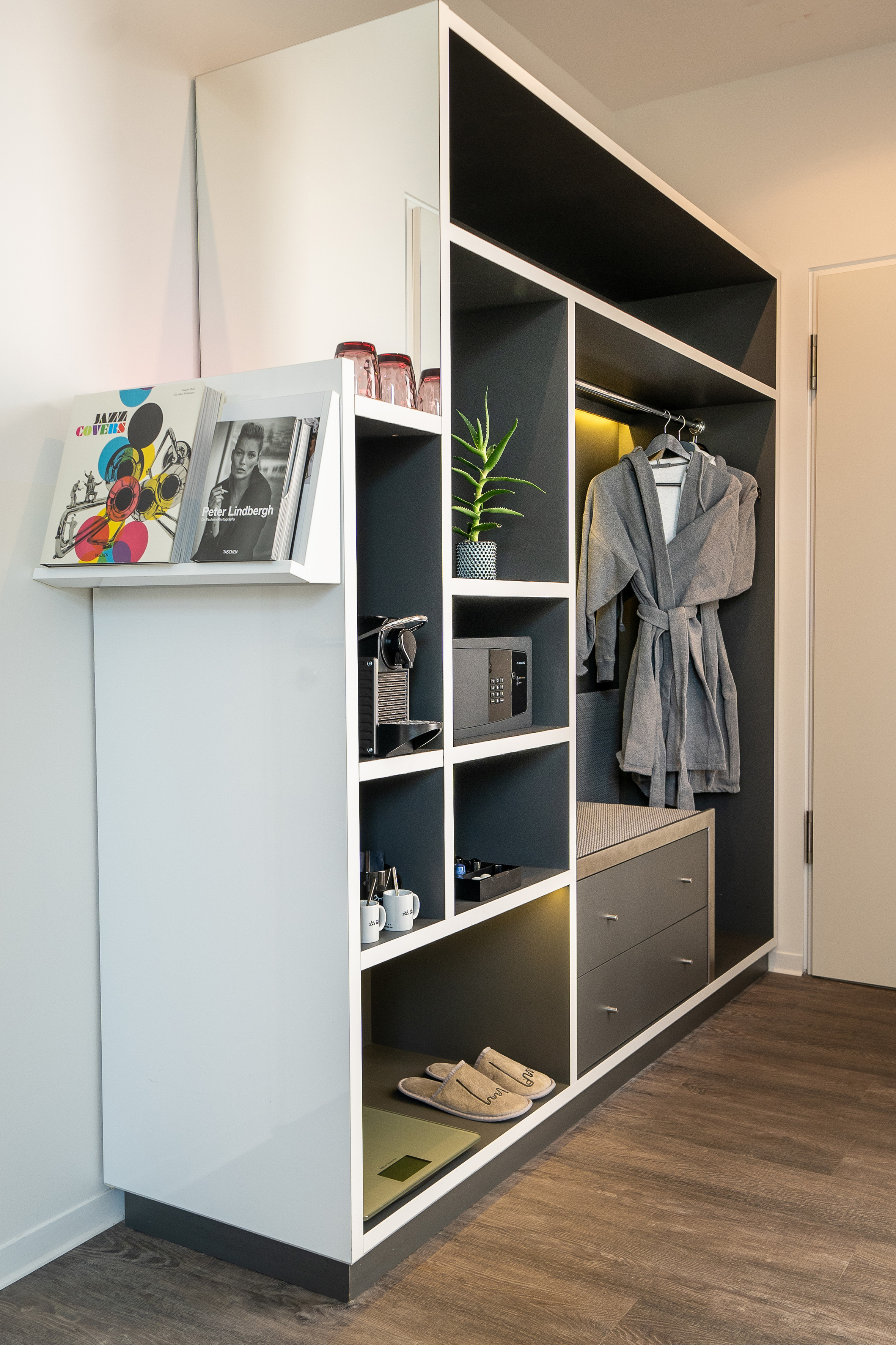 Stylish hotel room wardrobe with Nespresso, safe, bathrobes, slippers, and books.