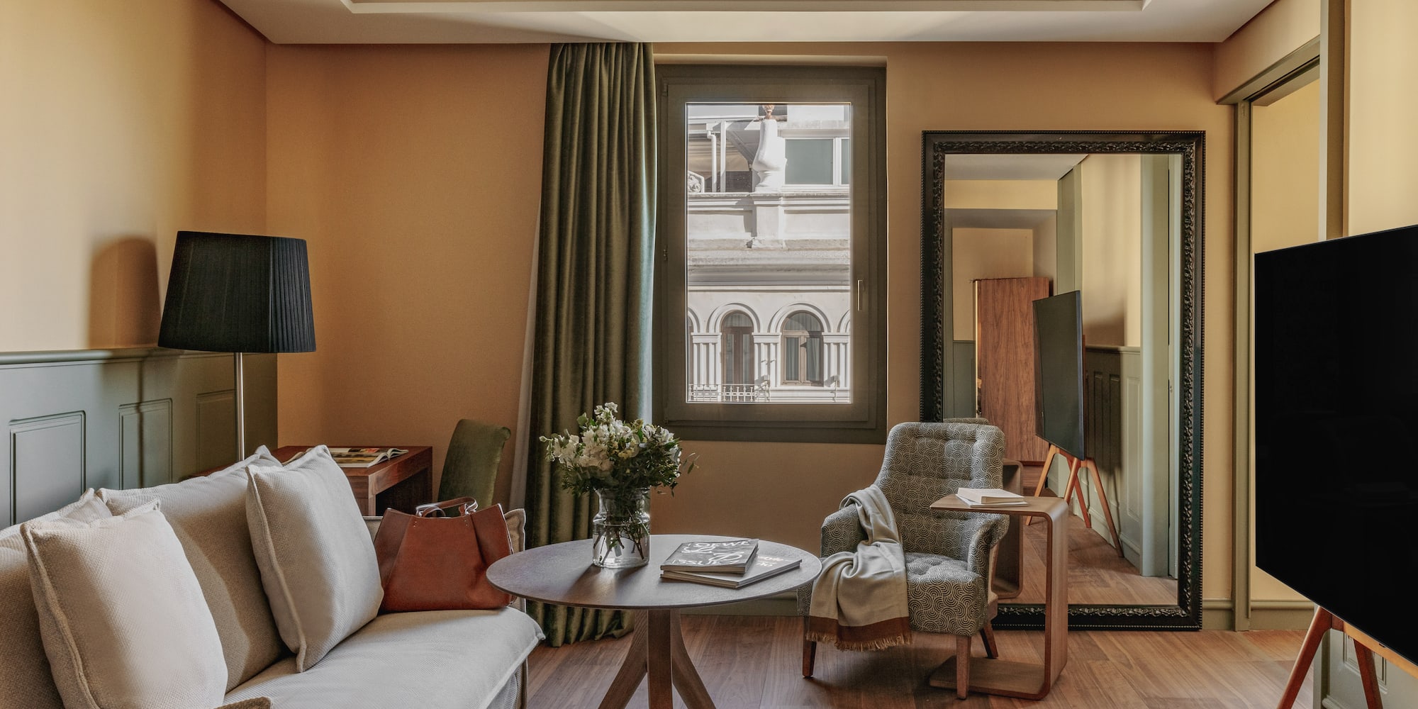 Diseño de suite de hotel con sofá, sillón, mesa, flores y ventana urbana.