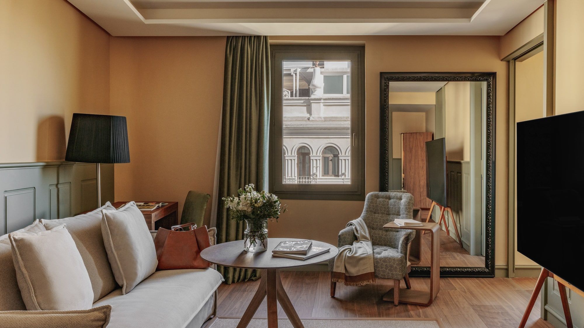 Diseño de suite de hotel con sofá, sillón, mesa, flores y ventana urbana.
