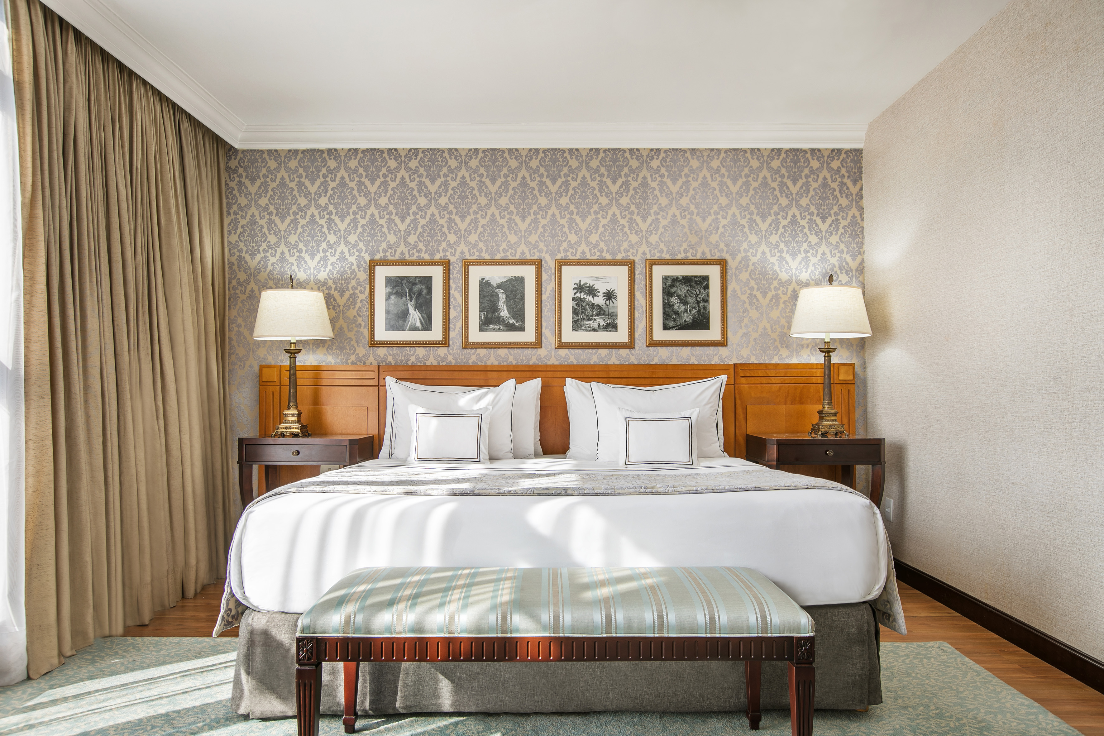 Elegant hotel bedroom, king bed, ornate wallpaper, framed art, bedside lamps.