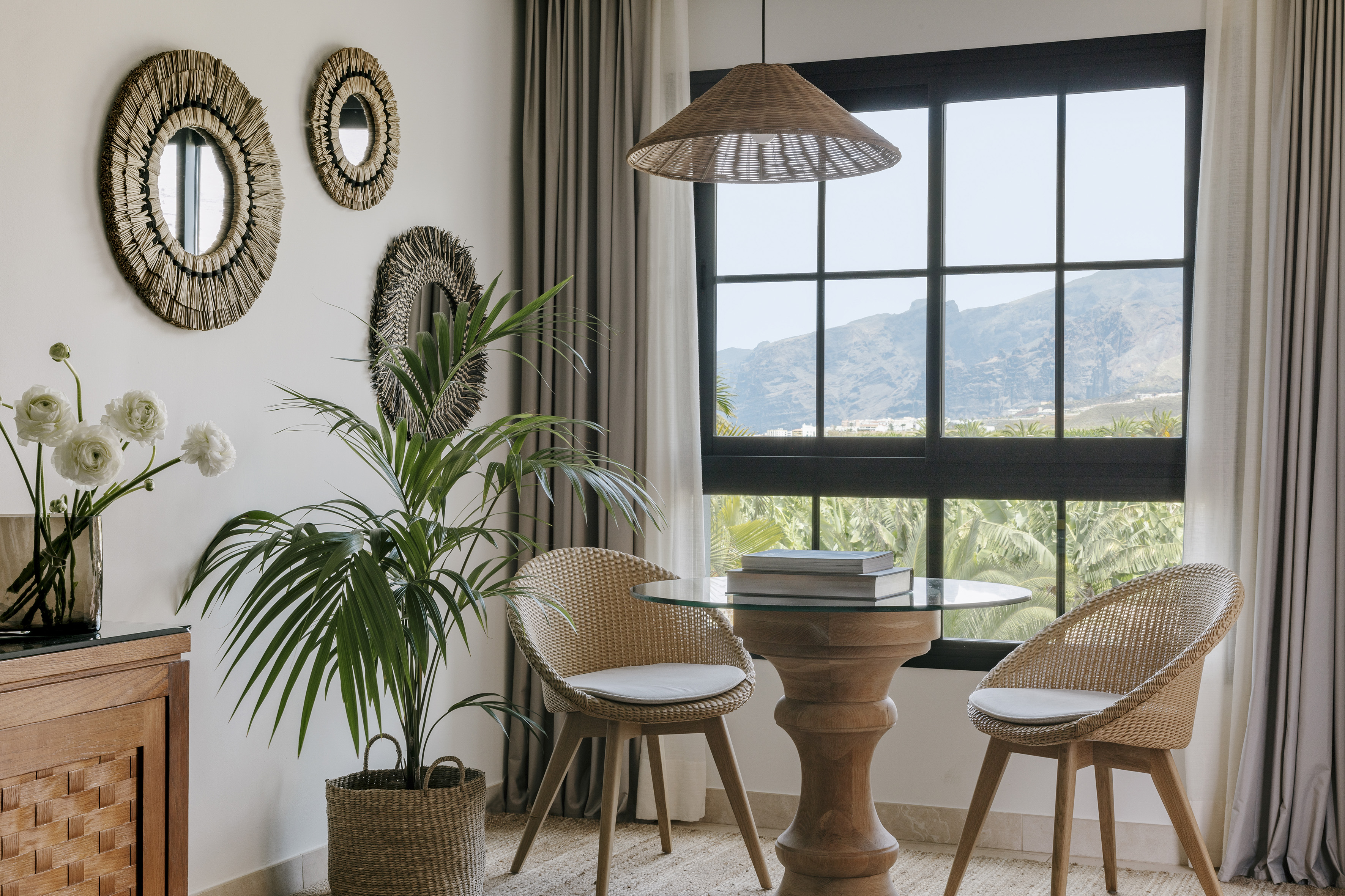 Rattan dining set by window with mountain view, tropical plant.