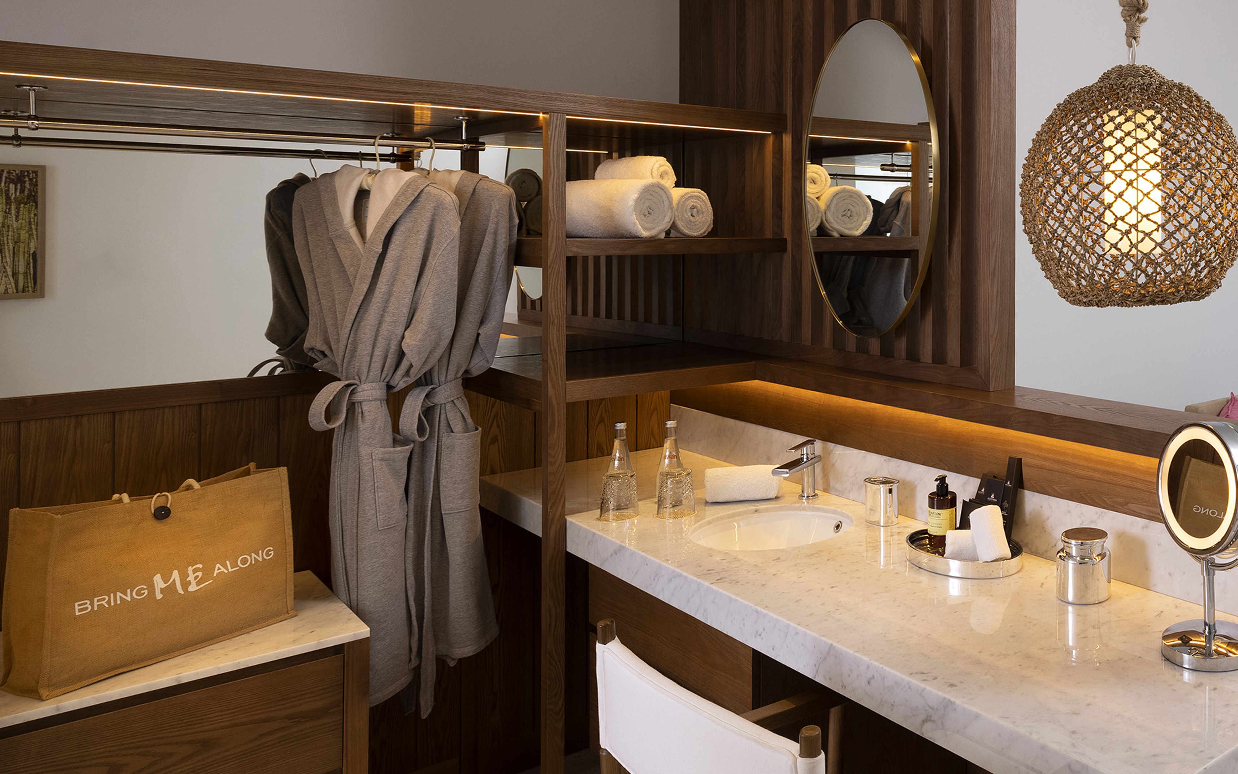 Hotel bathroom vanity with hanging robes, rolled towels, and marble countertop.