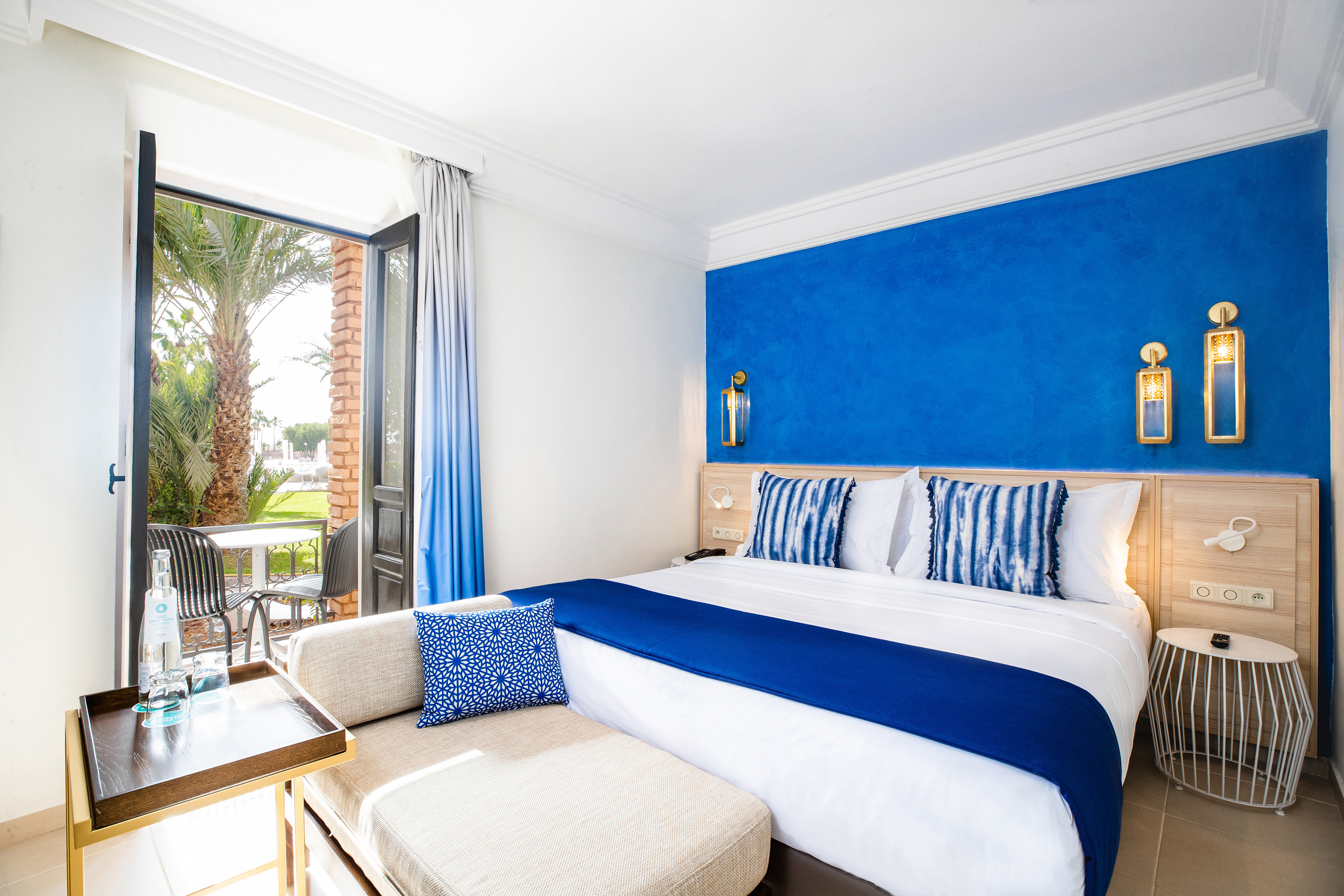 Modern hotel bedroom with blue accent wall, white bed, and balcony overlooking palm trees. - Sol Room cu balcon - SOL Oasis Marrakech, Marrakech
