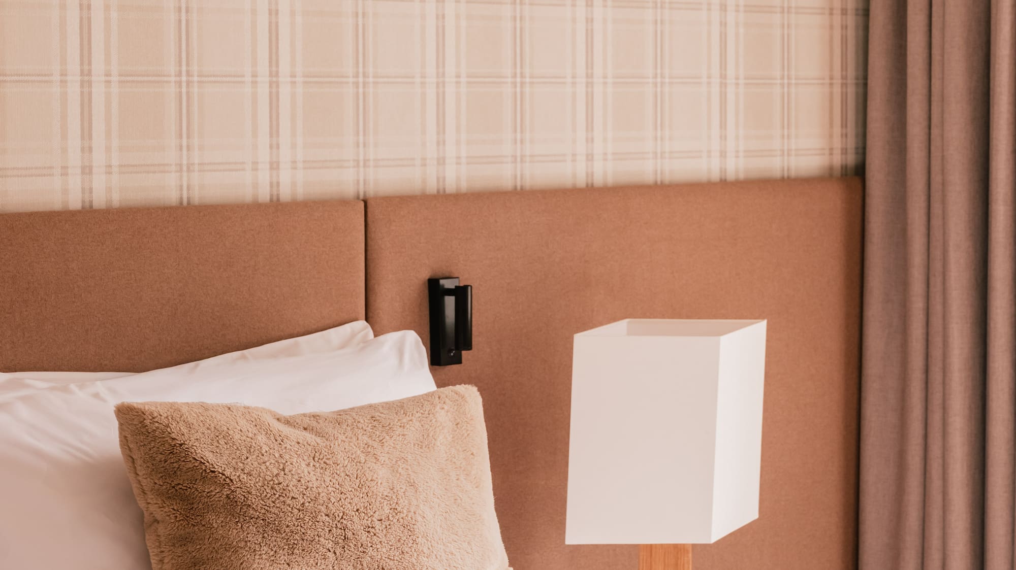 Cozy bedroom with plaid wallpaper, fluffy pillow, modern lamp, and natural decor.