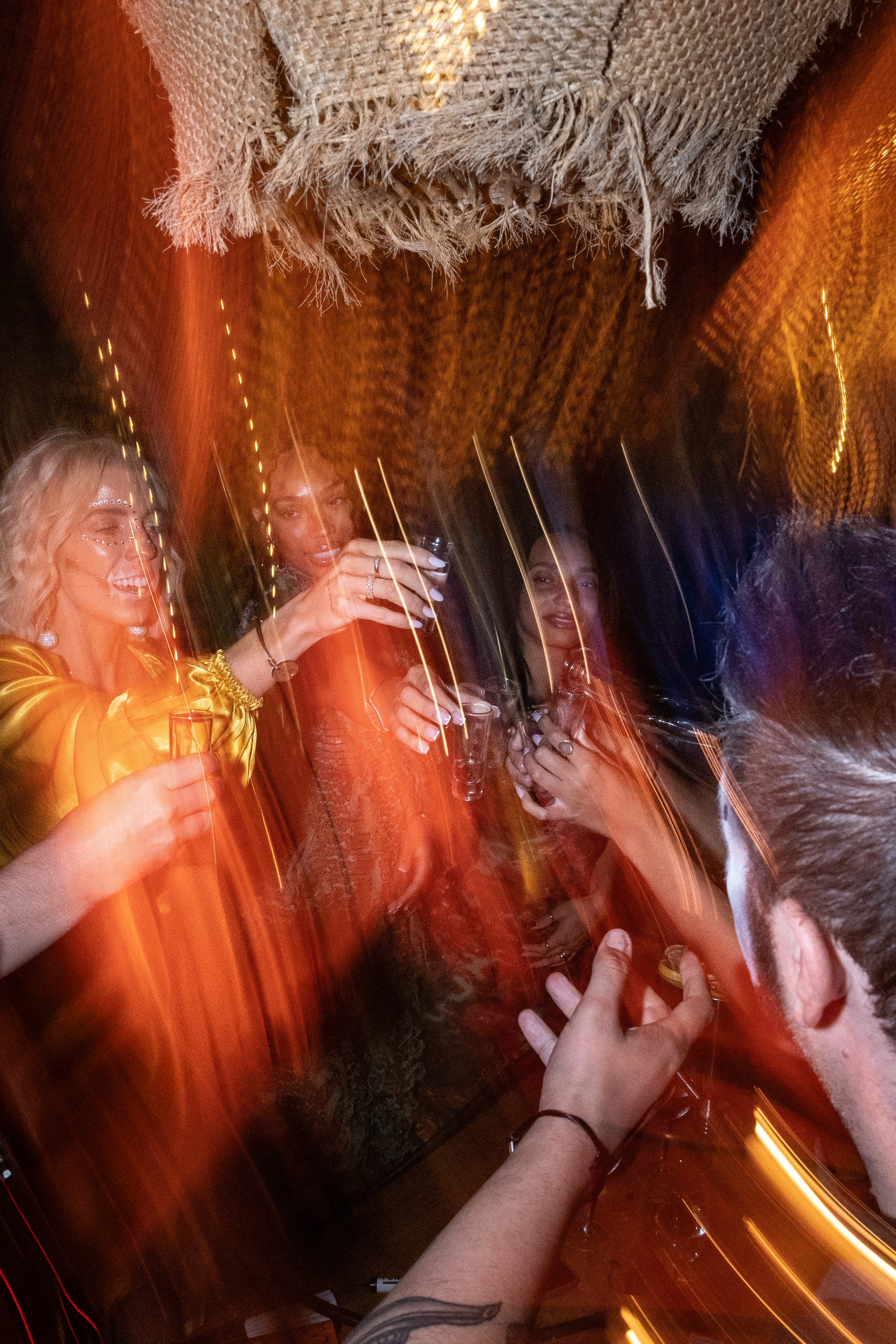 Friends toasting shots at a vibrant, blurred party with sparkling lights.