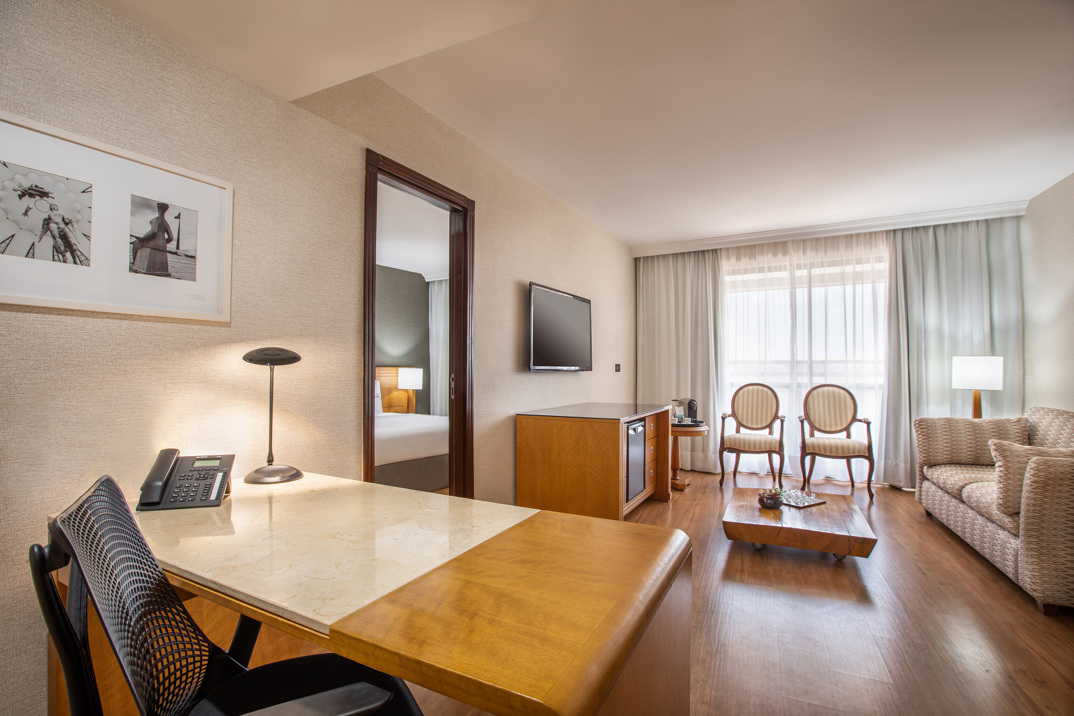 Modern hotel suite with comfortable living area, work desk, and bedroom view.