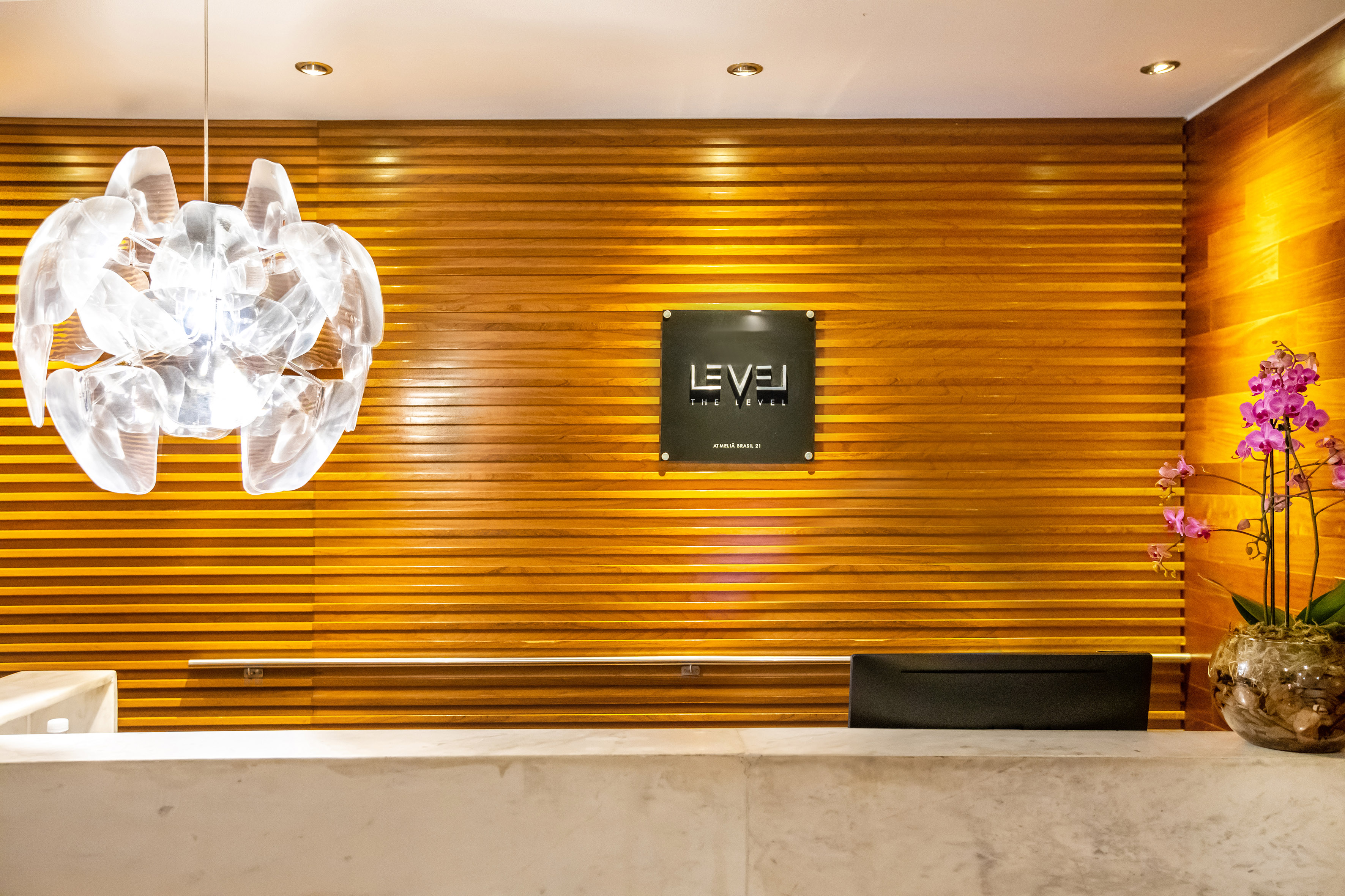 The Level Meliá Brasil 21 lobby: marble counter, wood wall, modern chandelier.
