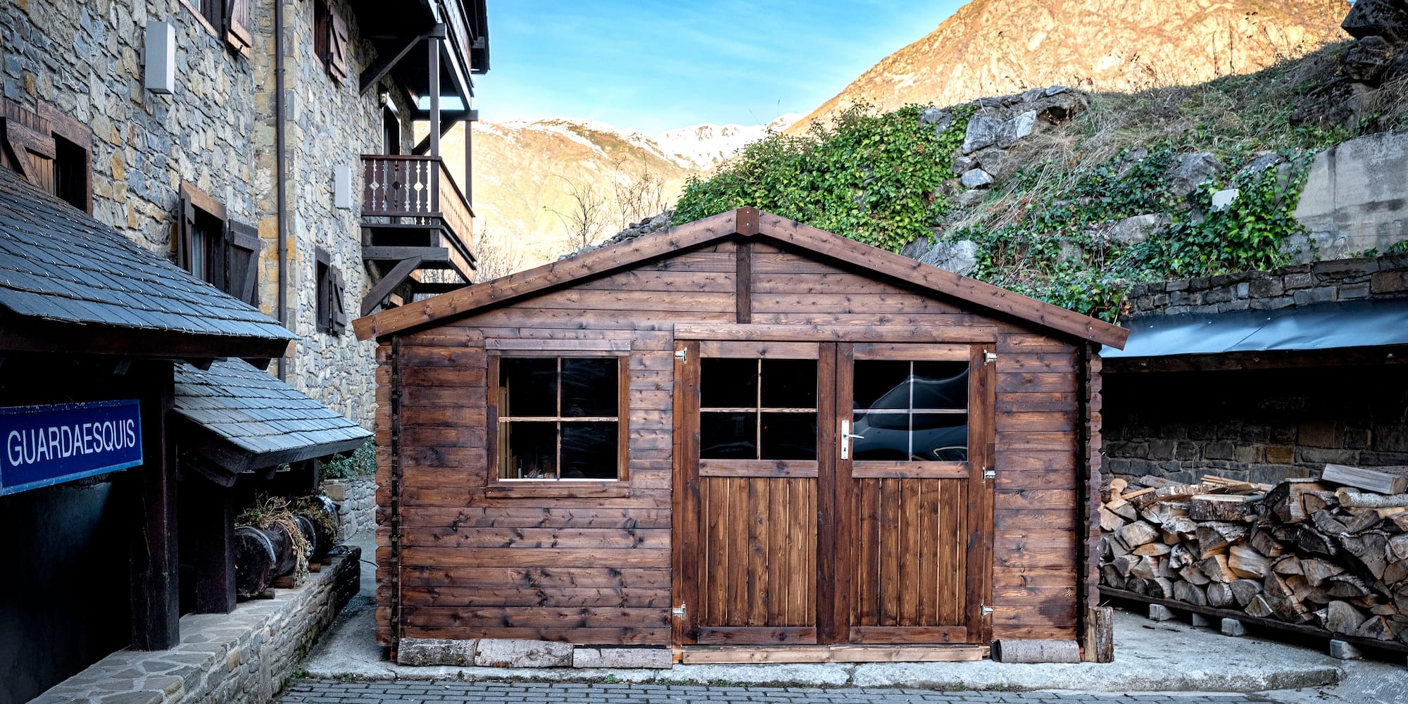 a wooden building with a stack of wood in front of a stone building