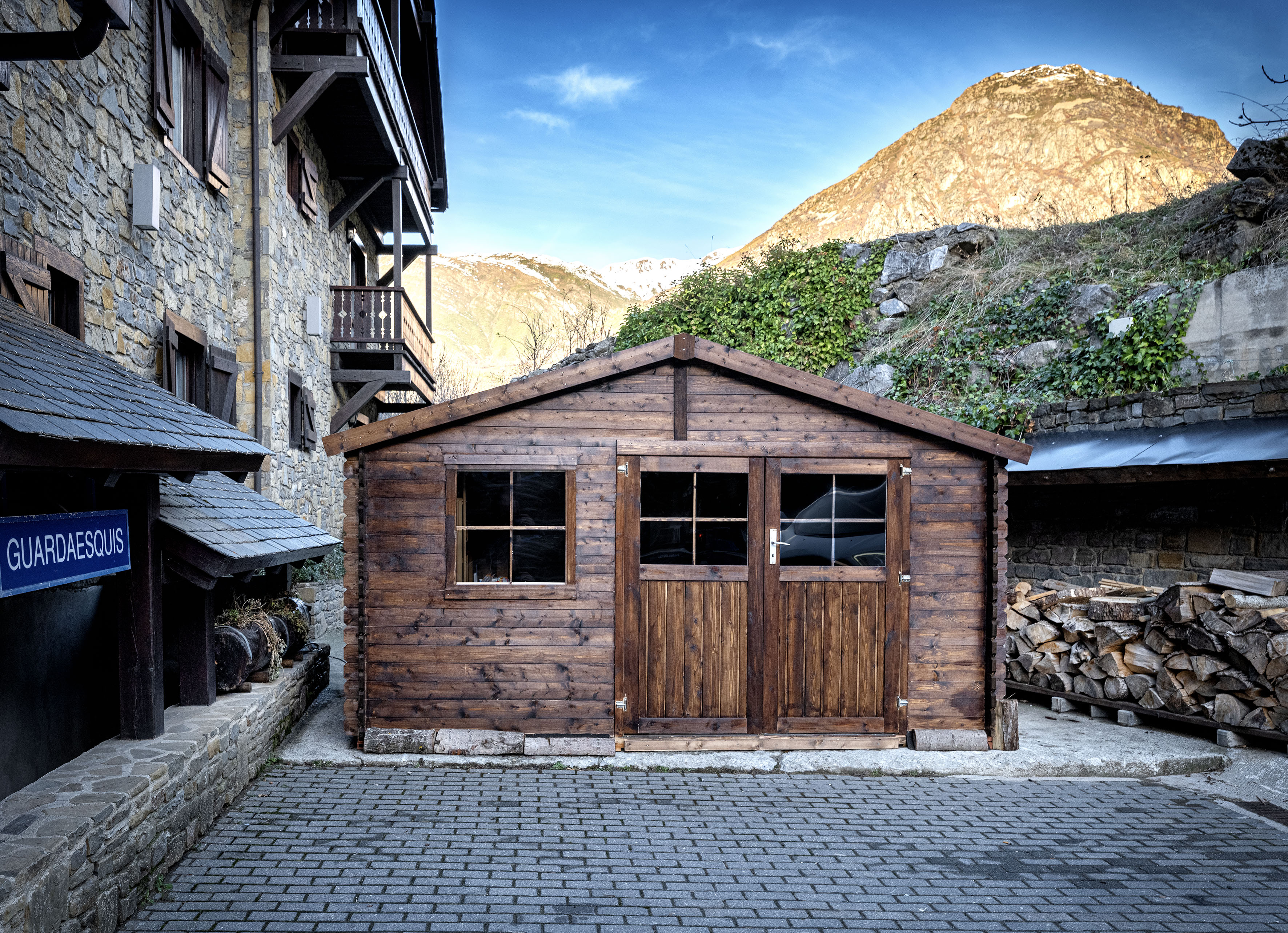a wooden building with a stack of wood in front of a stone building