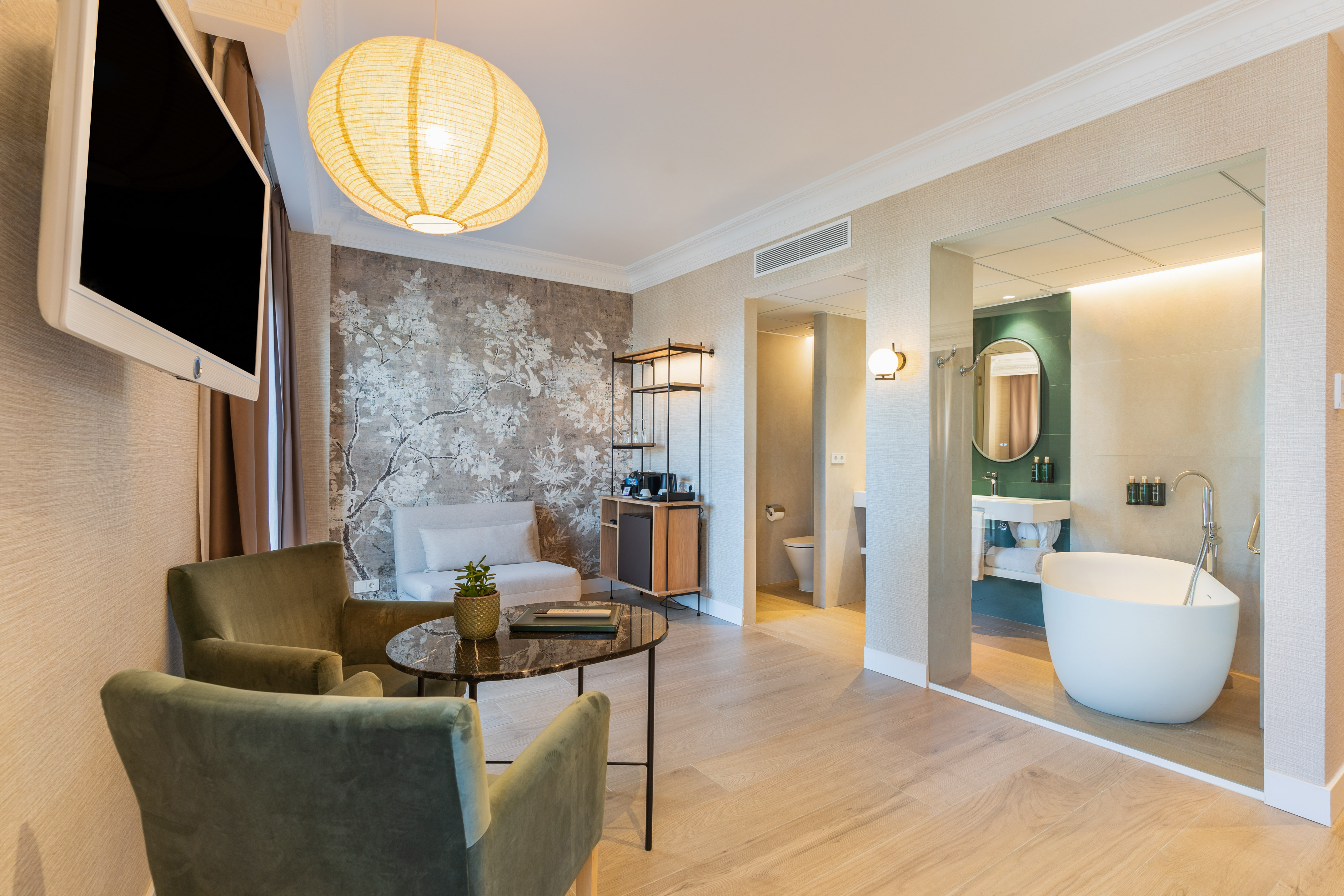 Hotel suite with modern living area, floral wall, and open bathroom with tub.