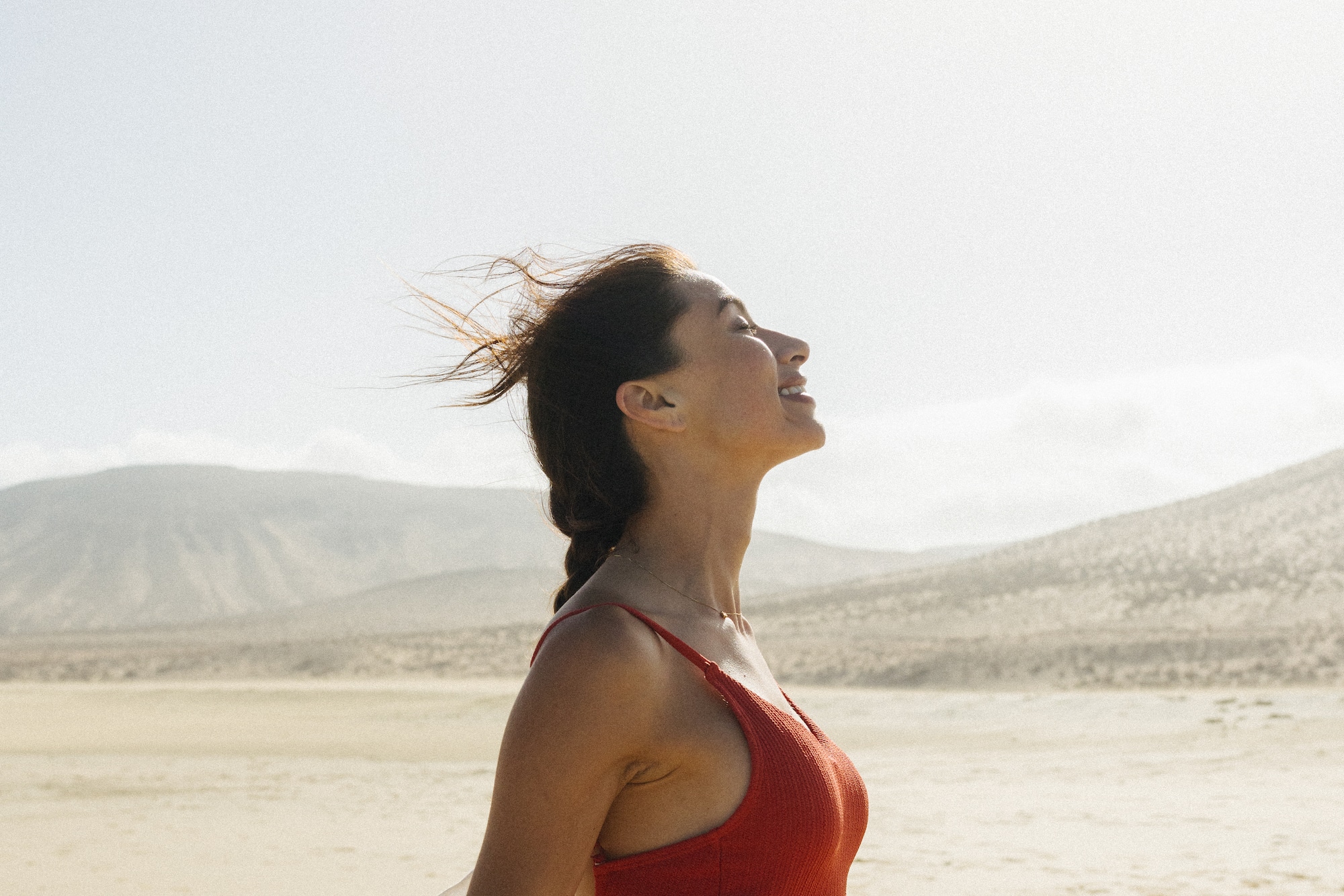 Mujer sonriente con blusa roja, cabello al viento en desierto.