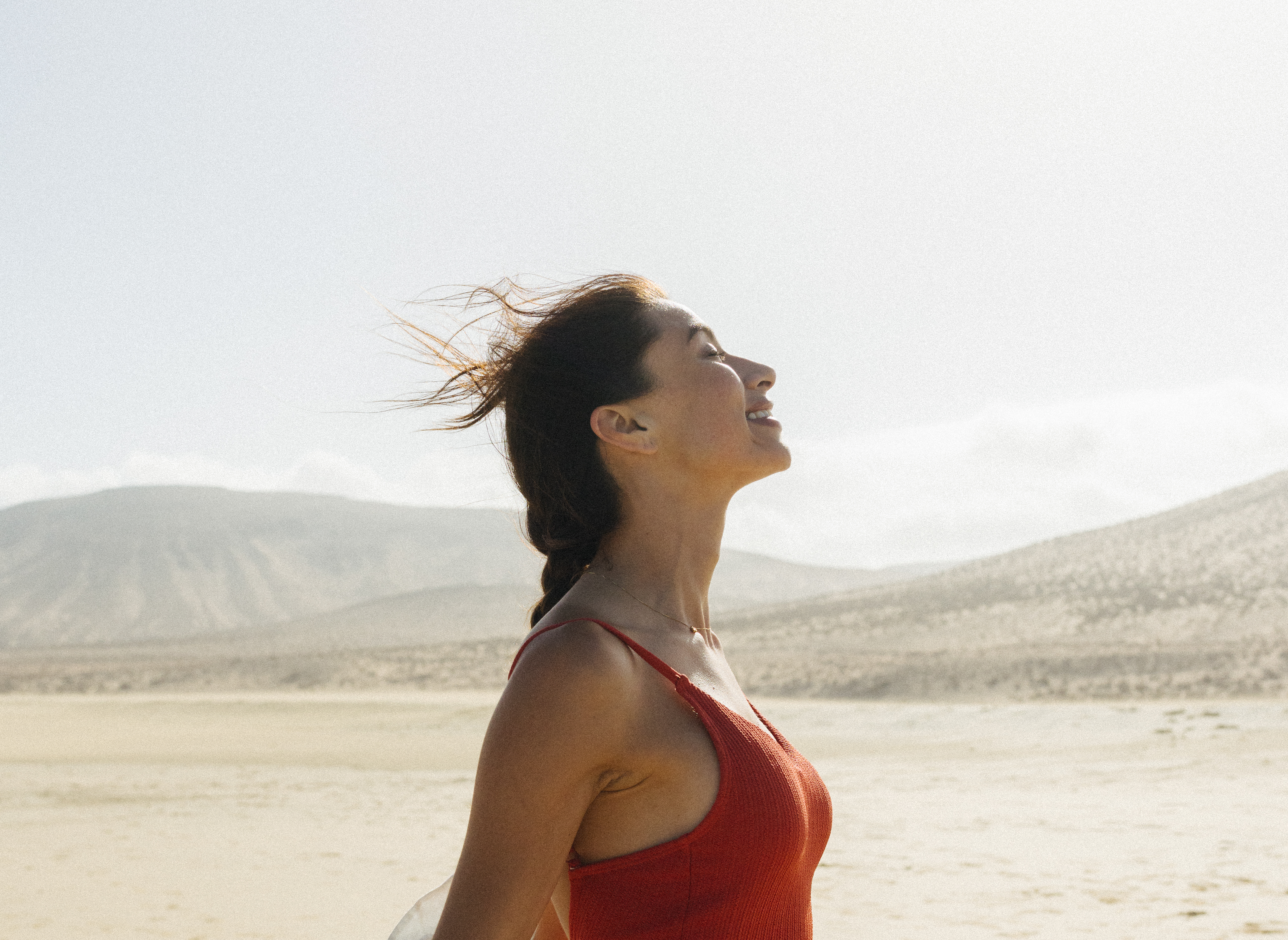 Mujer sonriente con blusa roja, cabello al viento en desierto.