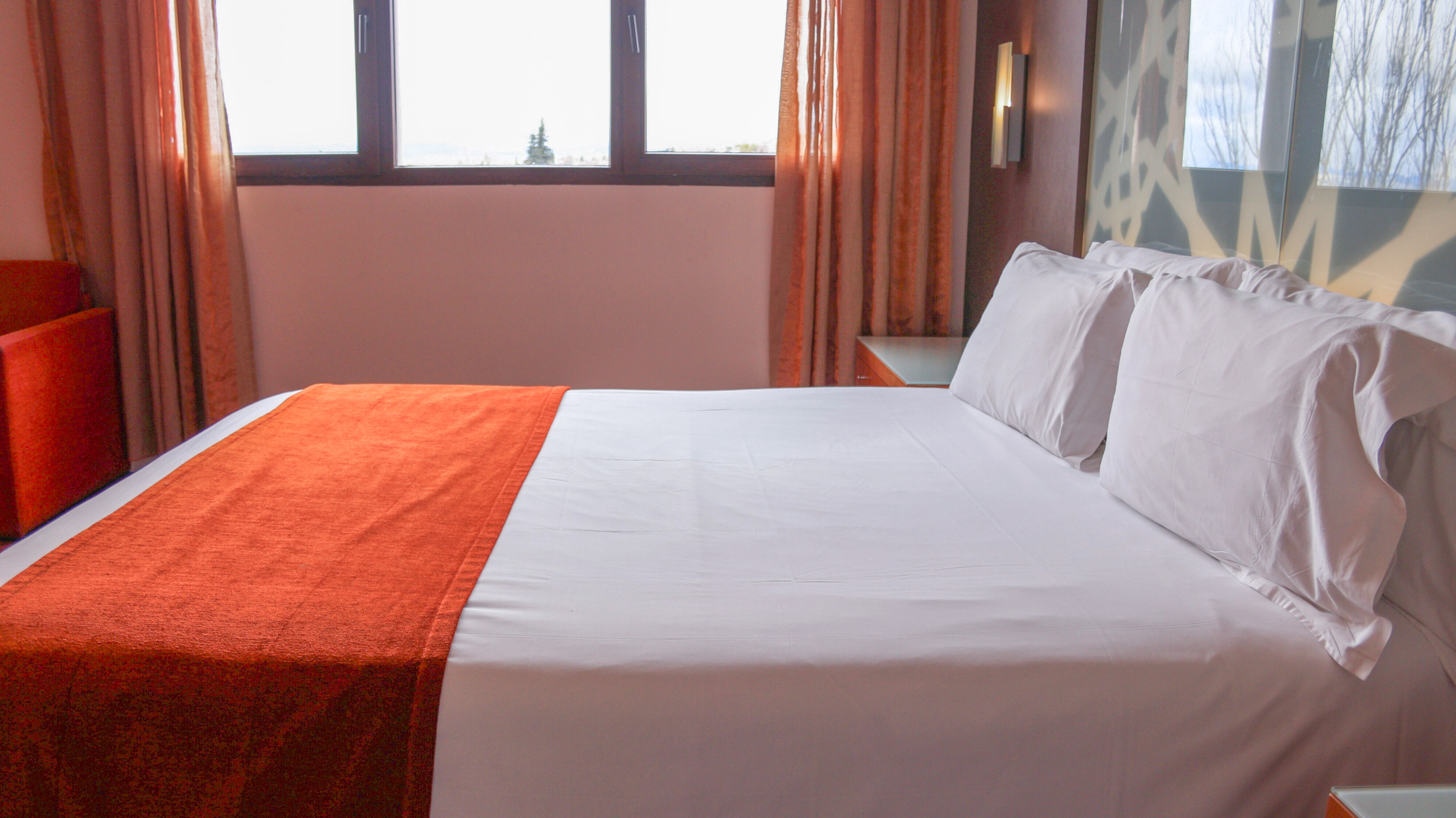 Comfortable hotel room with white bed, orange runner, and window.