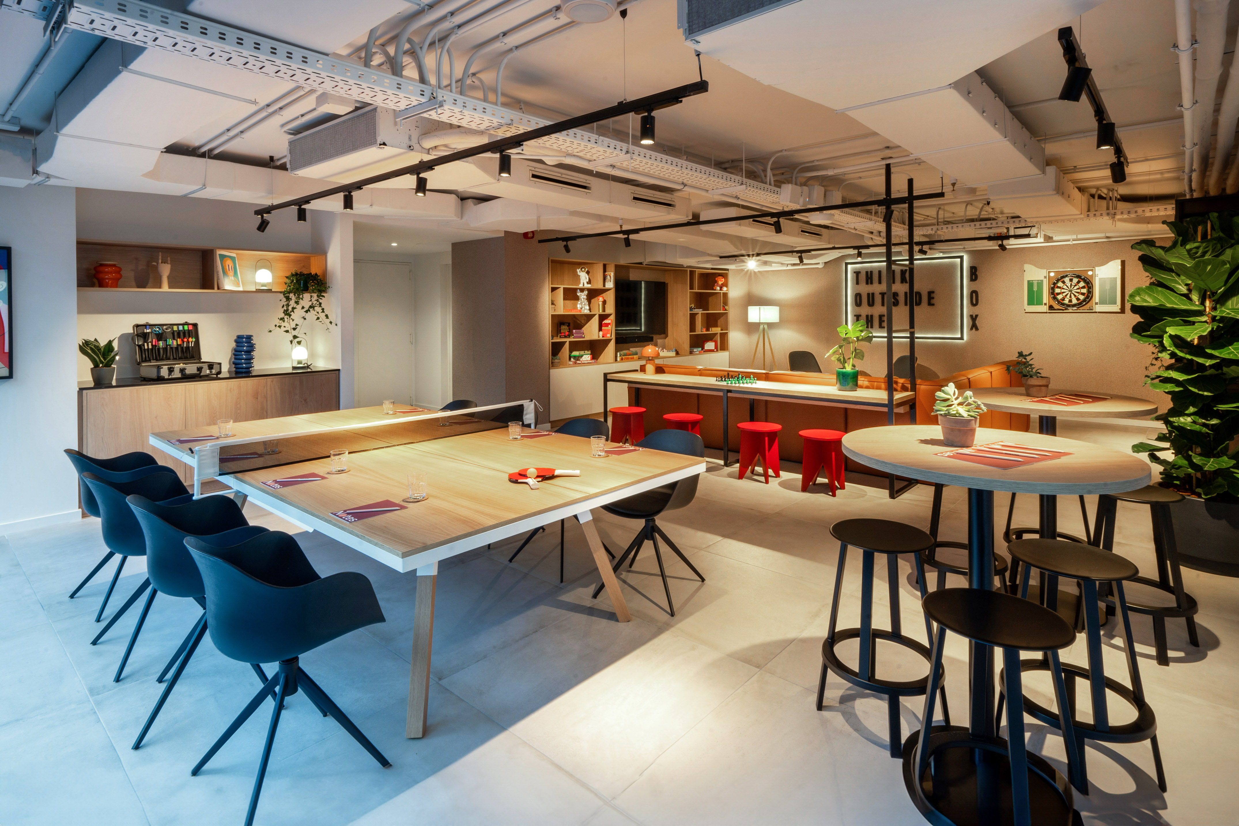 Modern office break room with ping pong table, dartboard, and lounge seating.