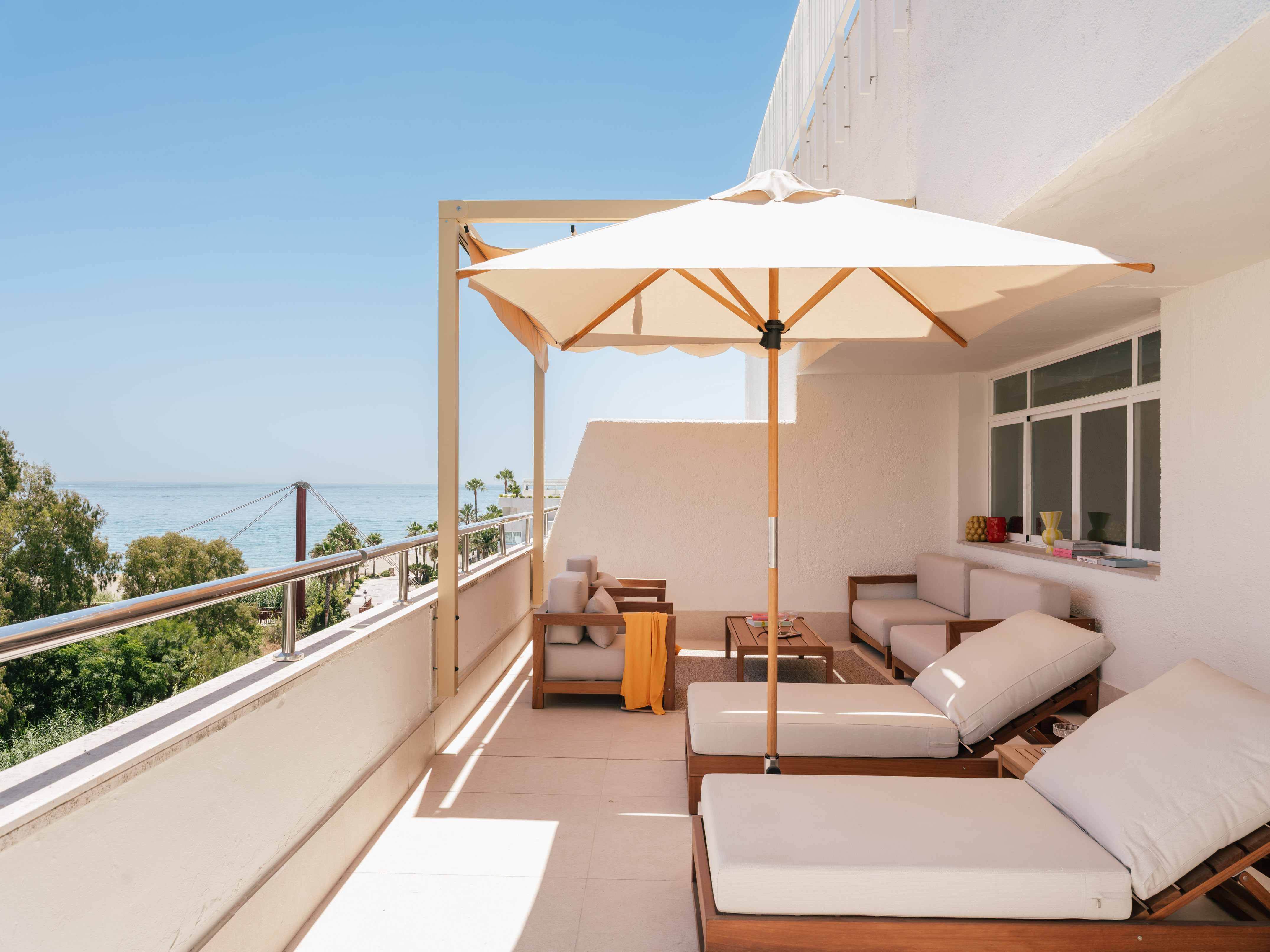 Modern balcony terrace with ocean view, wooden lounge chairs, and white parasol.