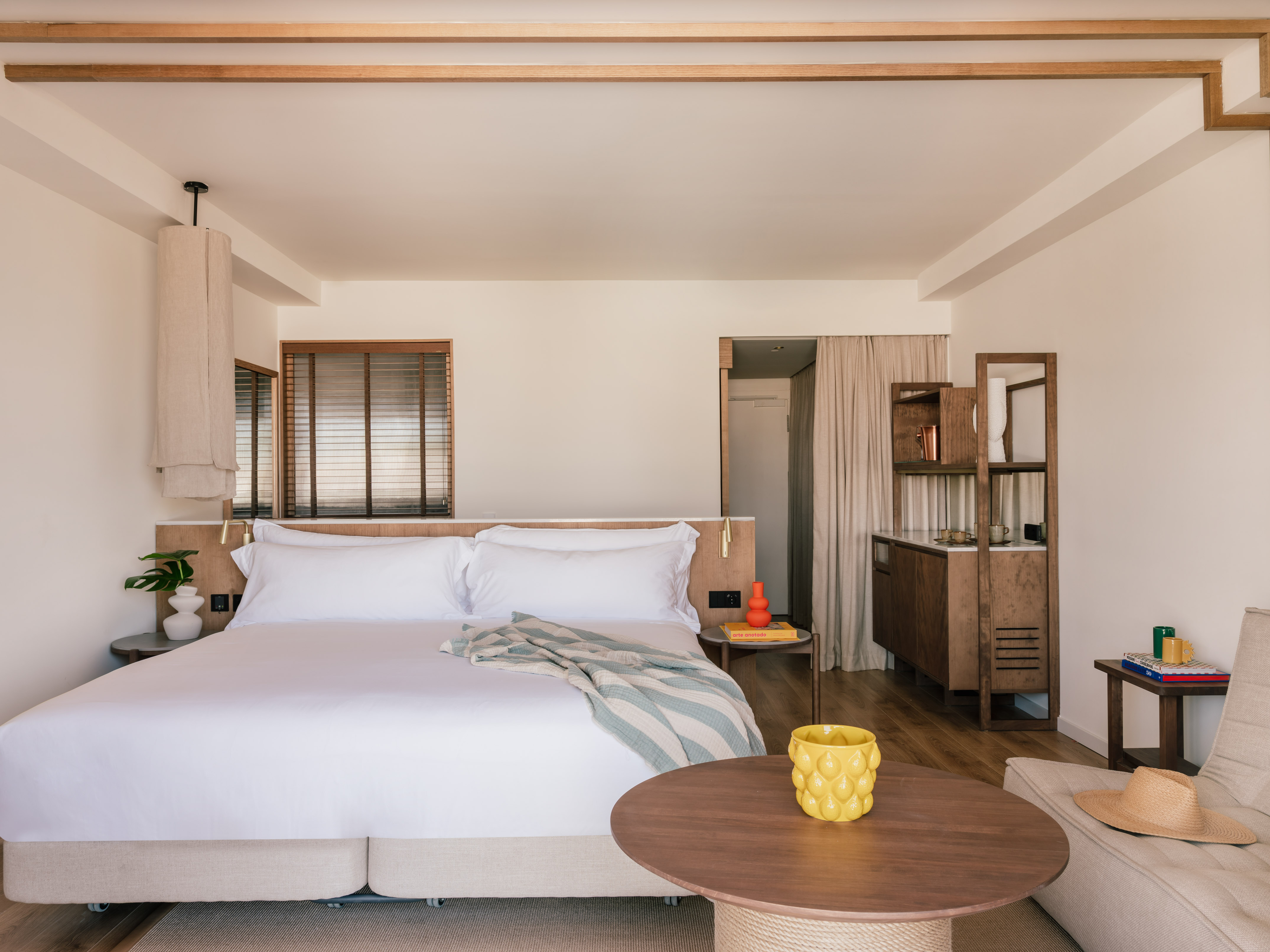 Contemporary hotel room with white bed, wooden accents, and light neutral decor.