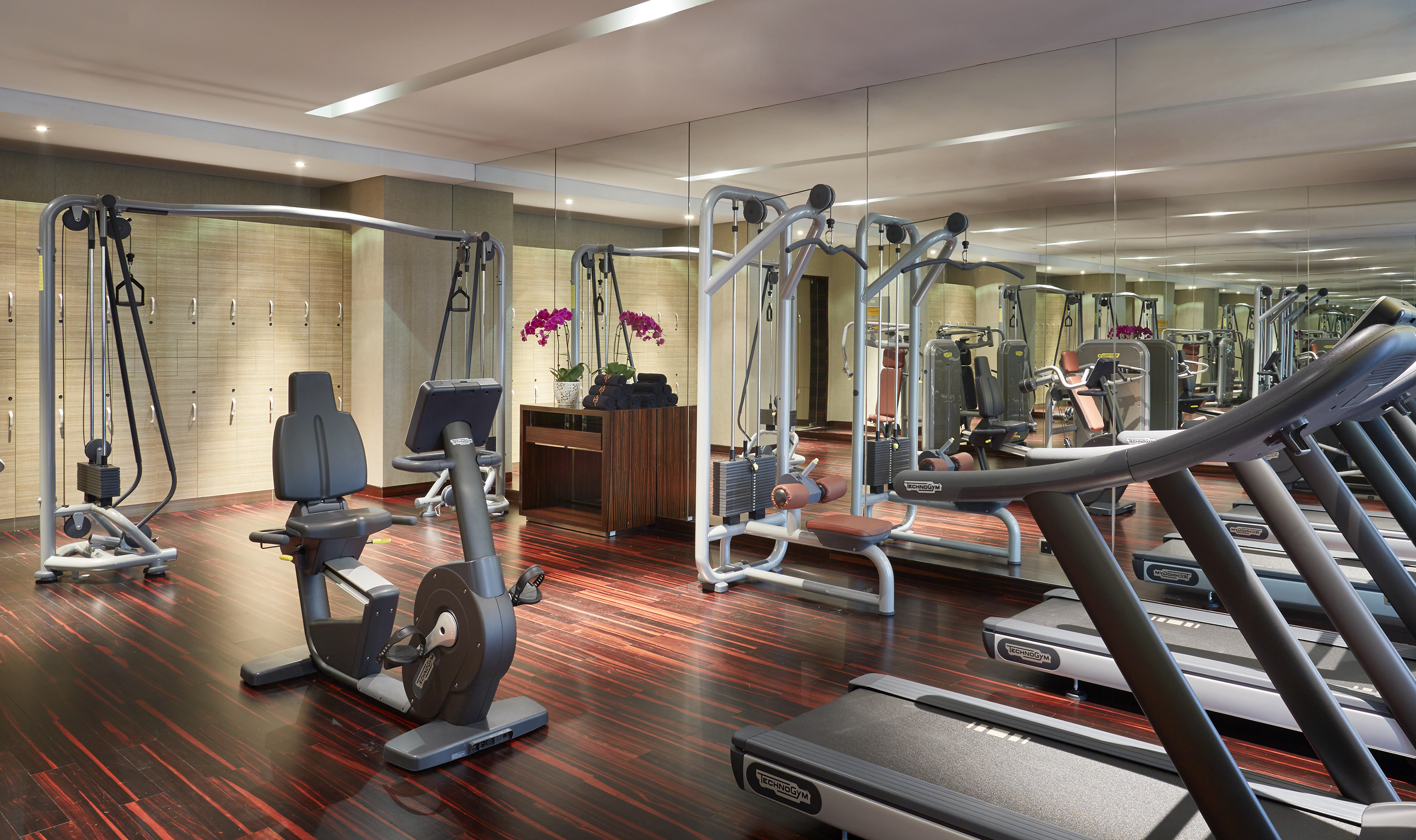 Technogym fitness center with treadmills, bike, weight machines, and wood floors.