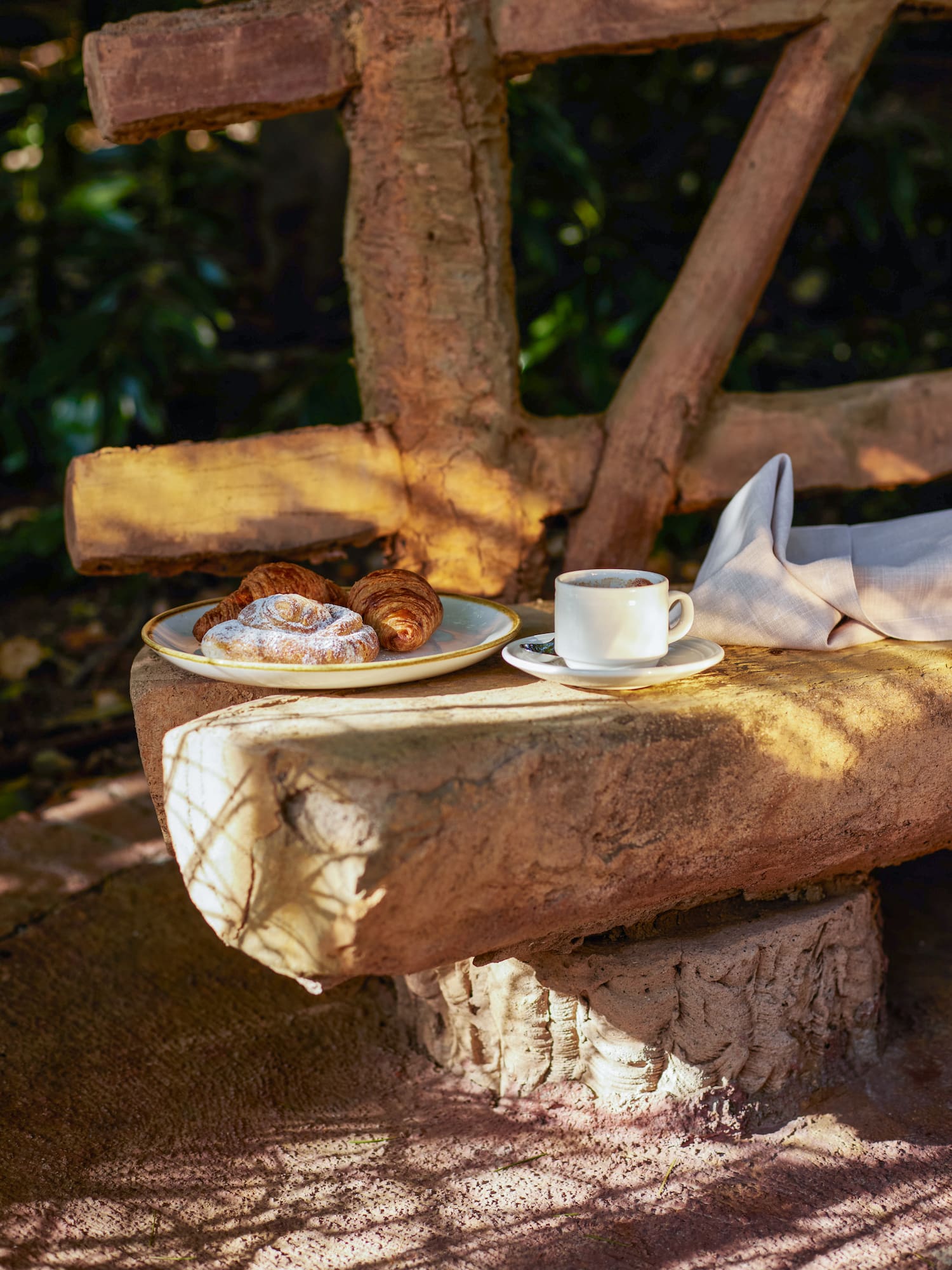 a plate of pastries and a cup of coffee on a stone bench