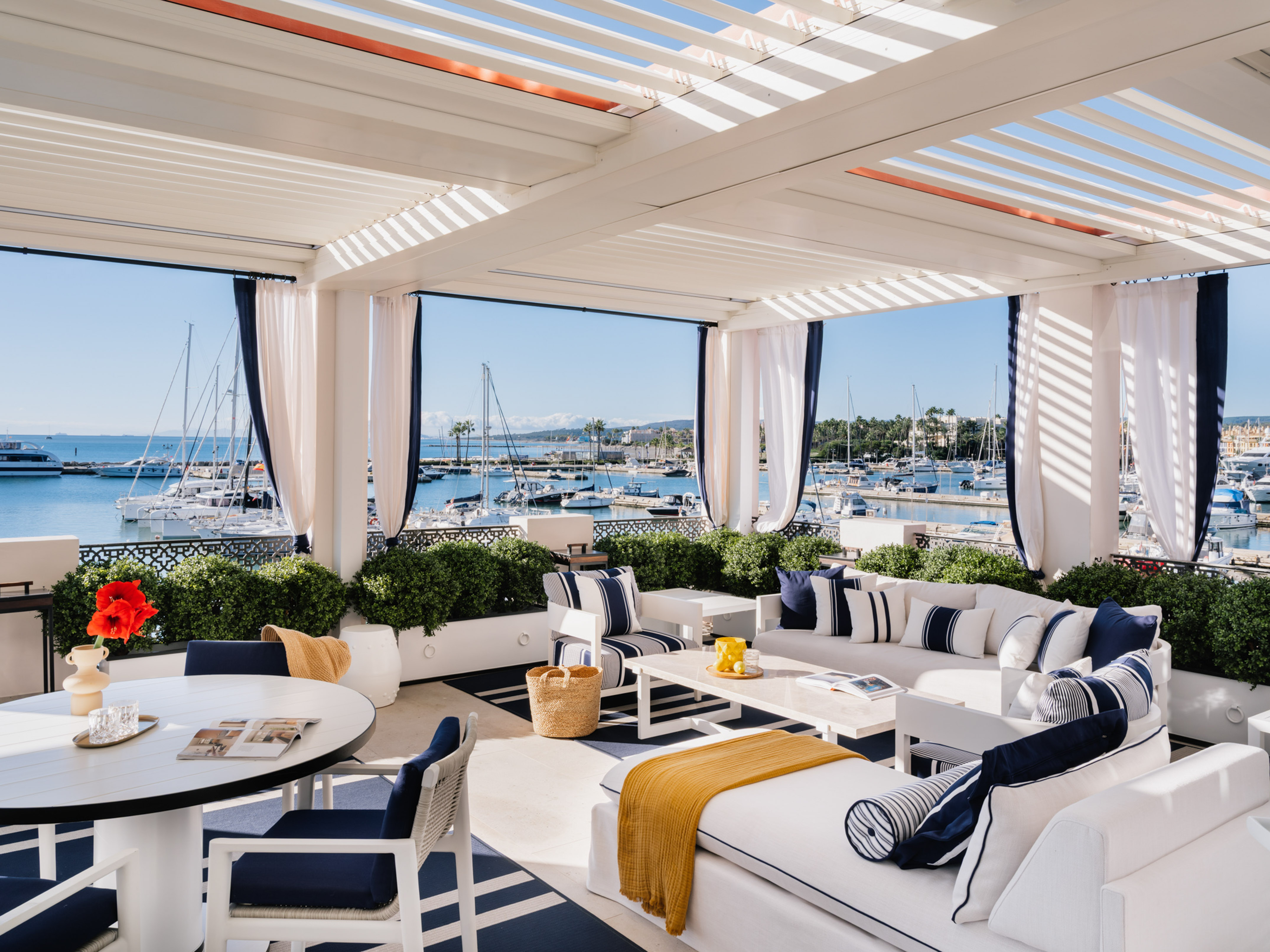 Luxury coastal patio with pergola, white furniture, and marina view.