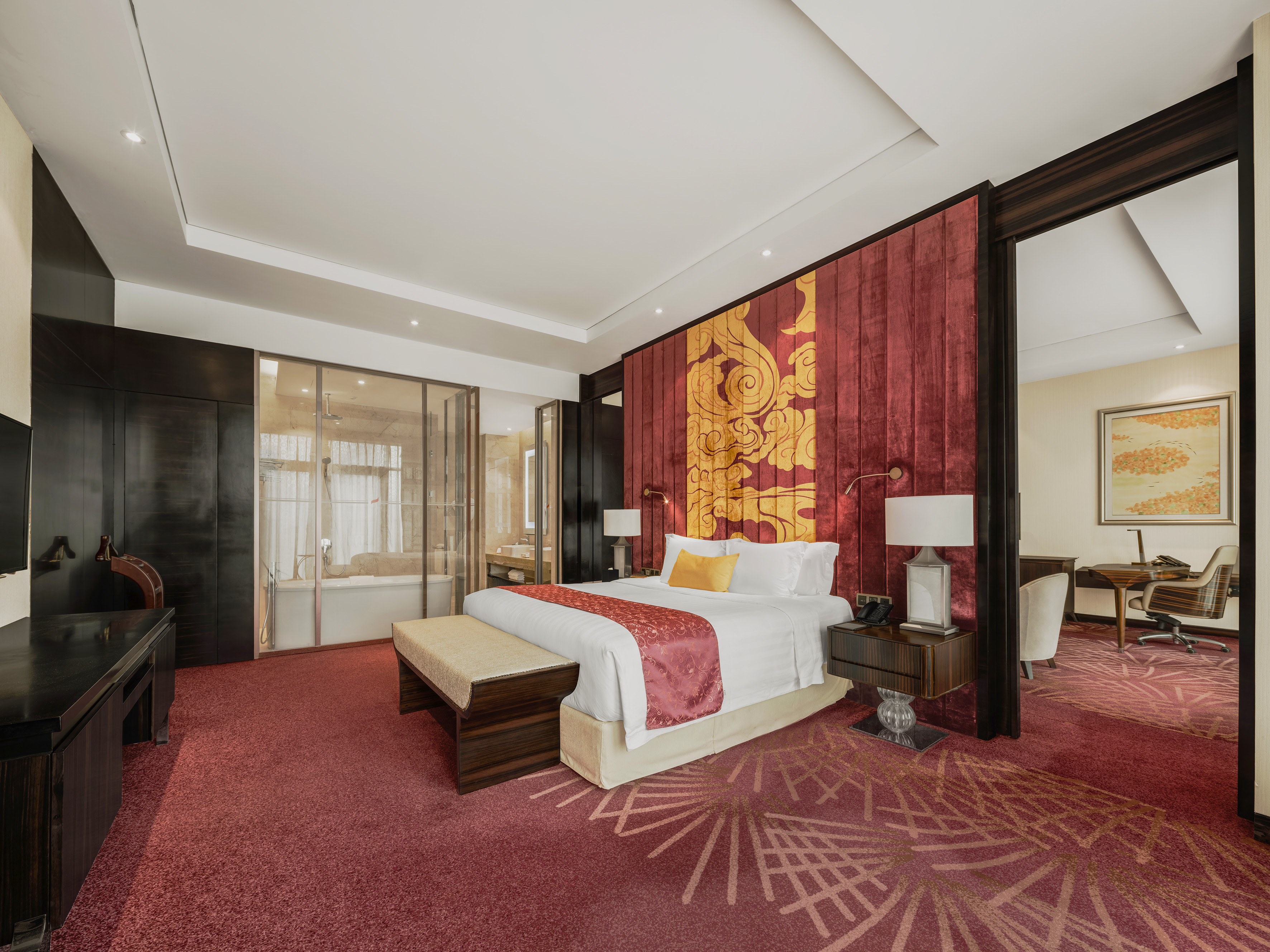 Elegant hotel suite with red and gold Asian-inspired decor, king bed, and office nook.