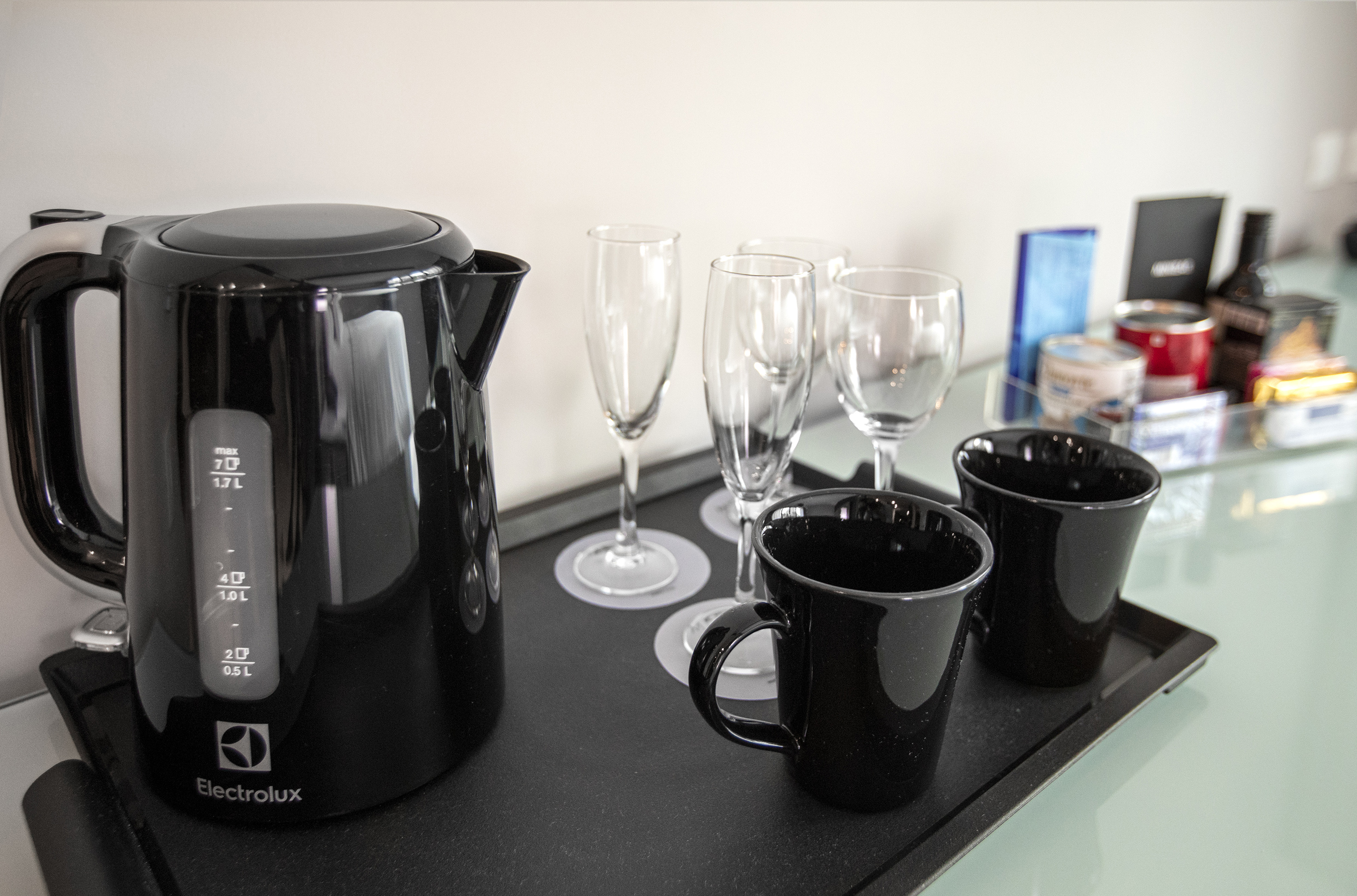 Black Electrolux kettle, champagne flutes, and mugs on a hotel mini-bar tray.