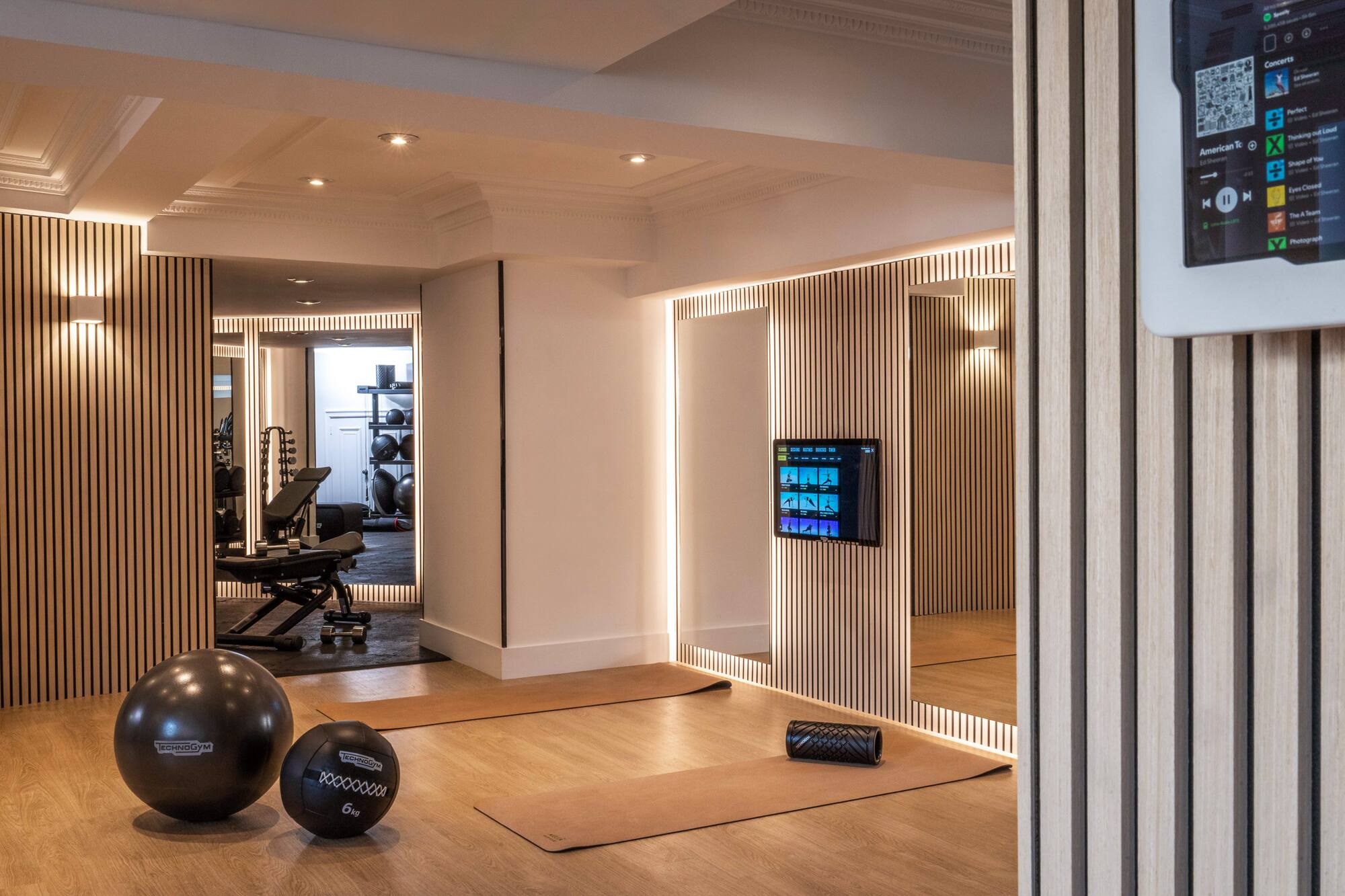 Modern home gym design with wood slats, yoga mats, and Technogym equipment.