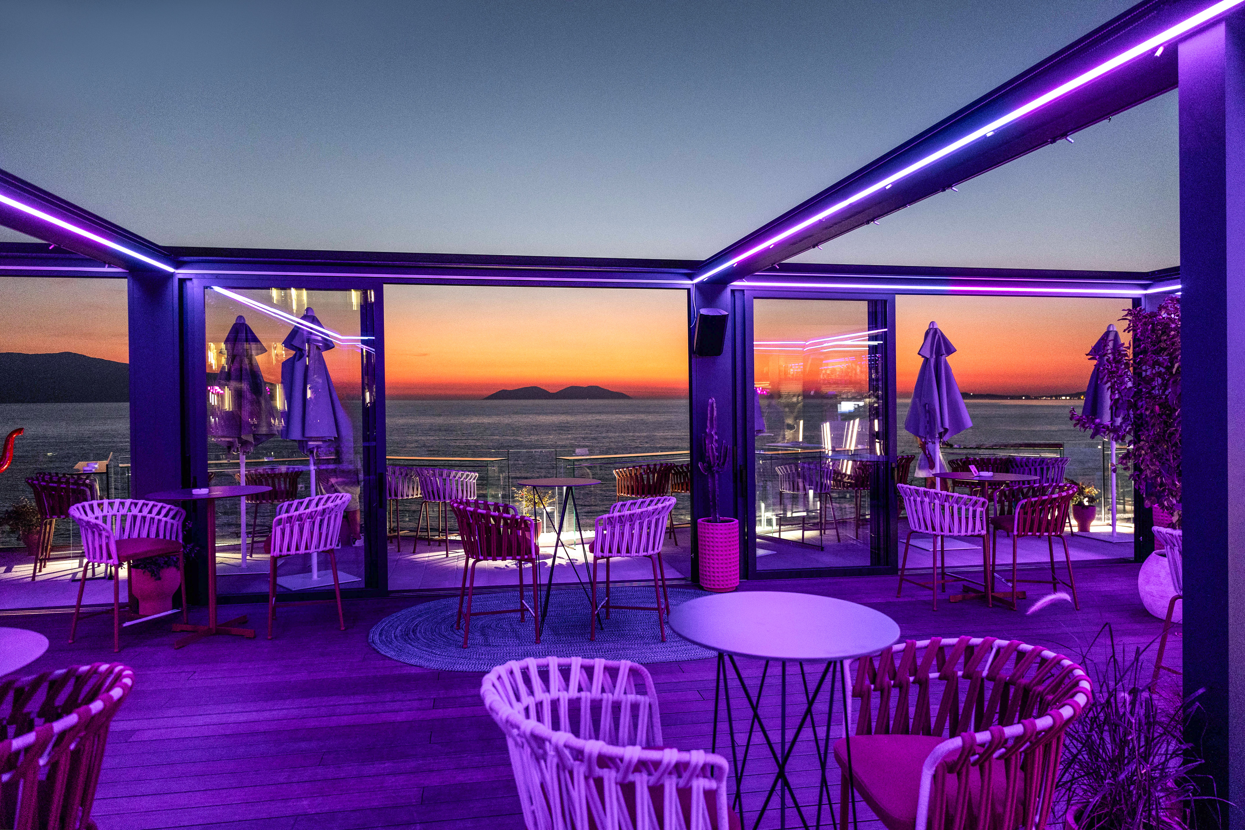 Outdoor bar terrace with purple neon lights and sunset sea view.