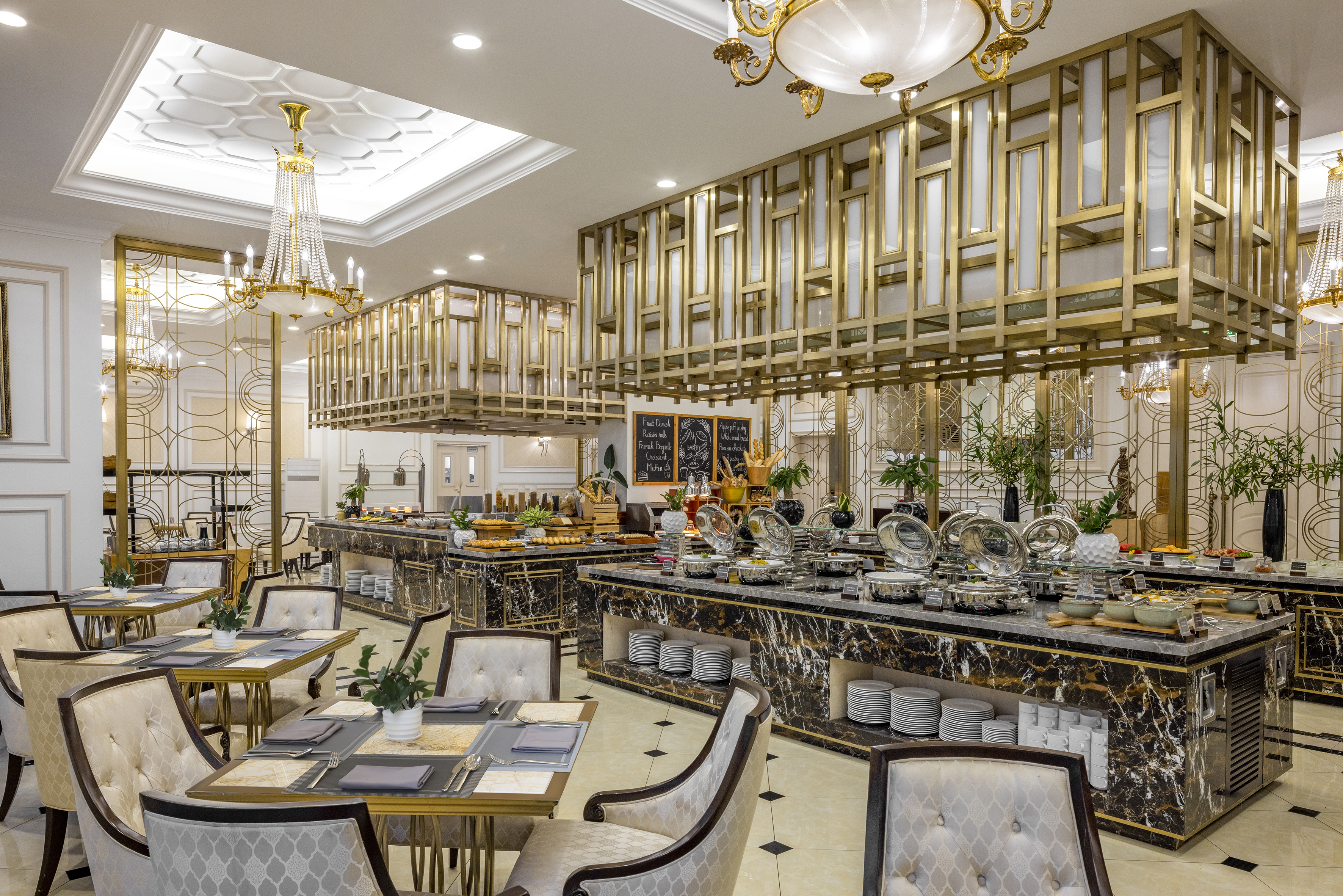 Elegant hotel buffet with gold-accented marble counters and set dining tables.